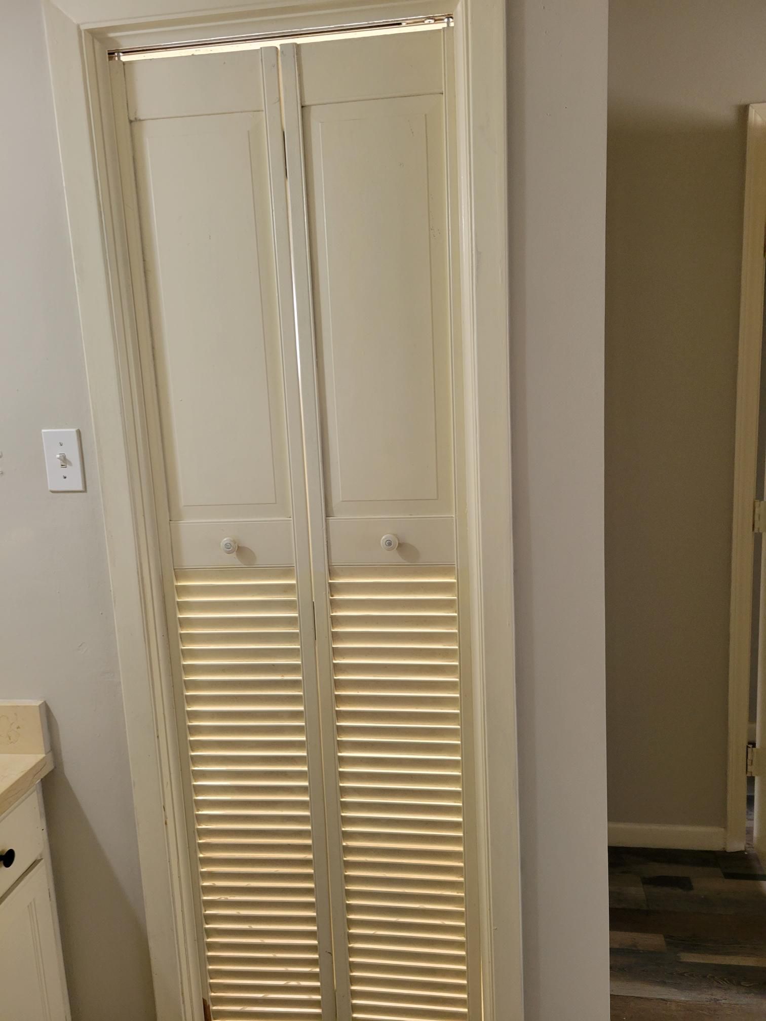 Closed, cream-colored bi-fold closet doors with slatted lower portion; set against a light gray wall.
