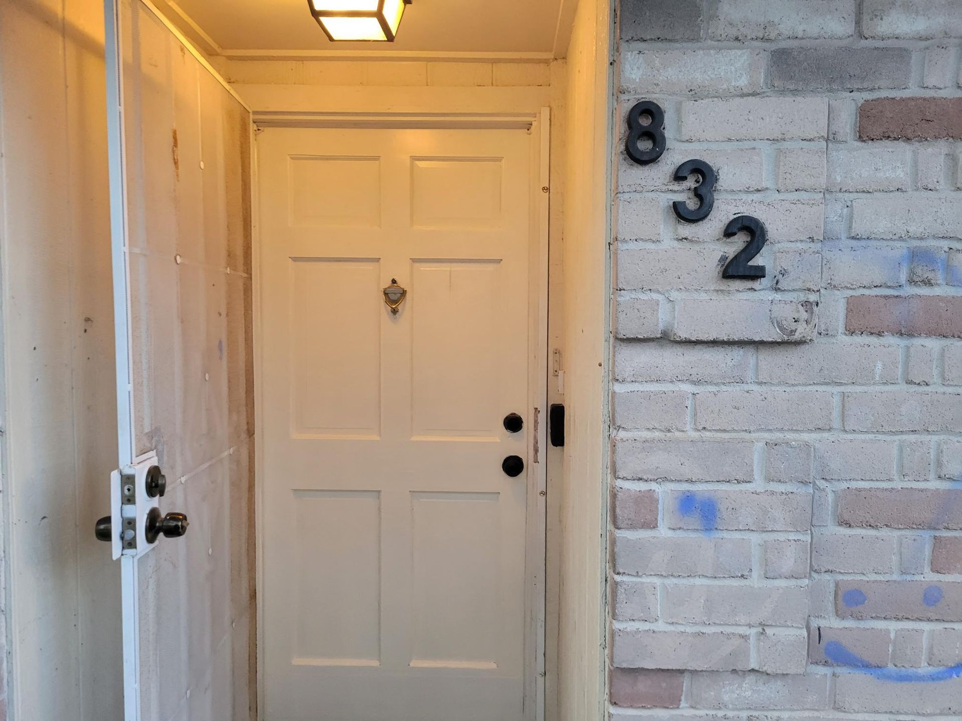 White front door with a knocker, beside a brick wall with the number 832.