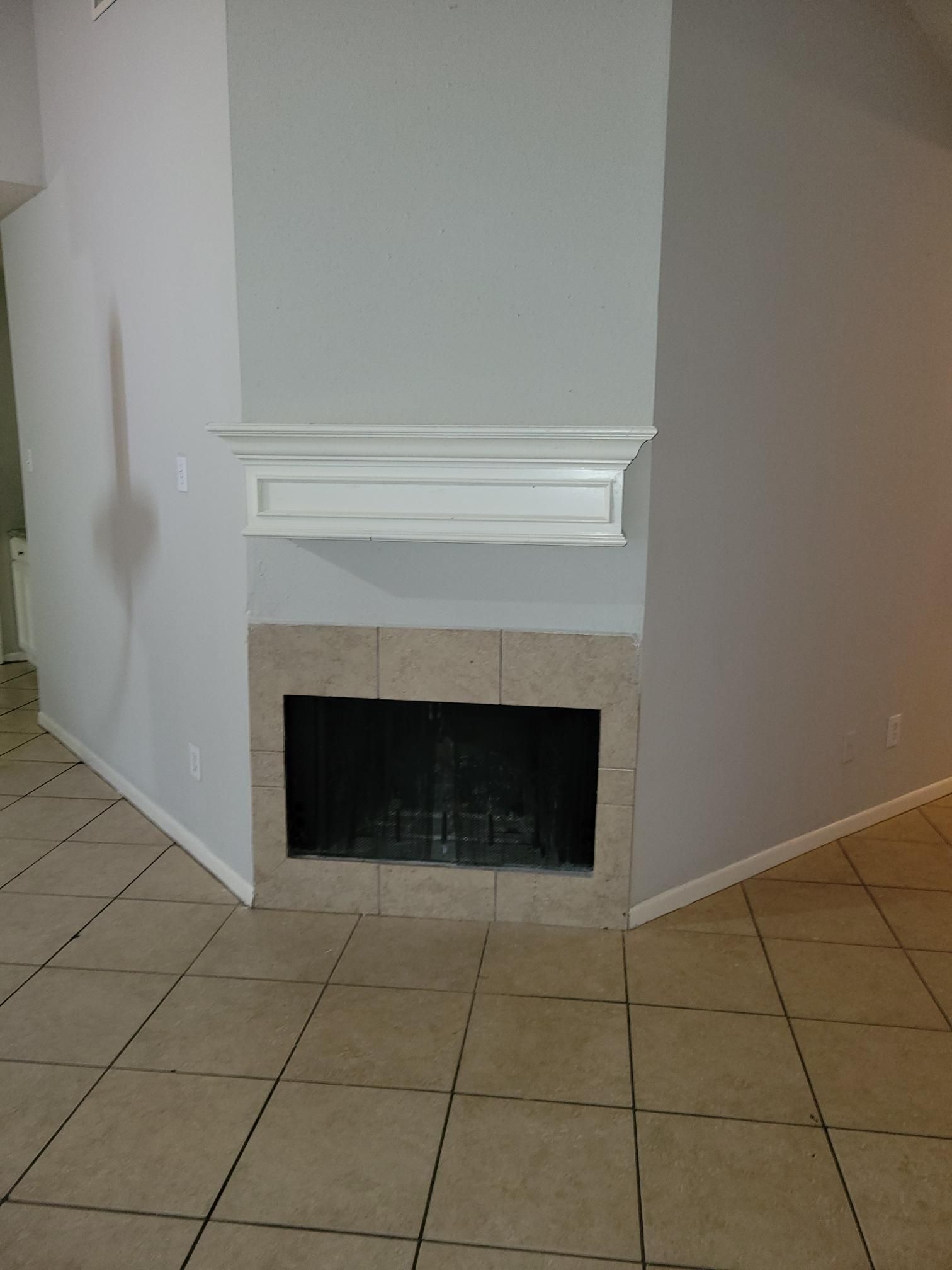 Fireplace with cream tile, white mantle, and gray walls in a room with beige tile flooring.