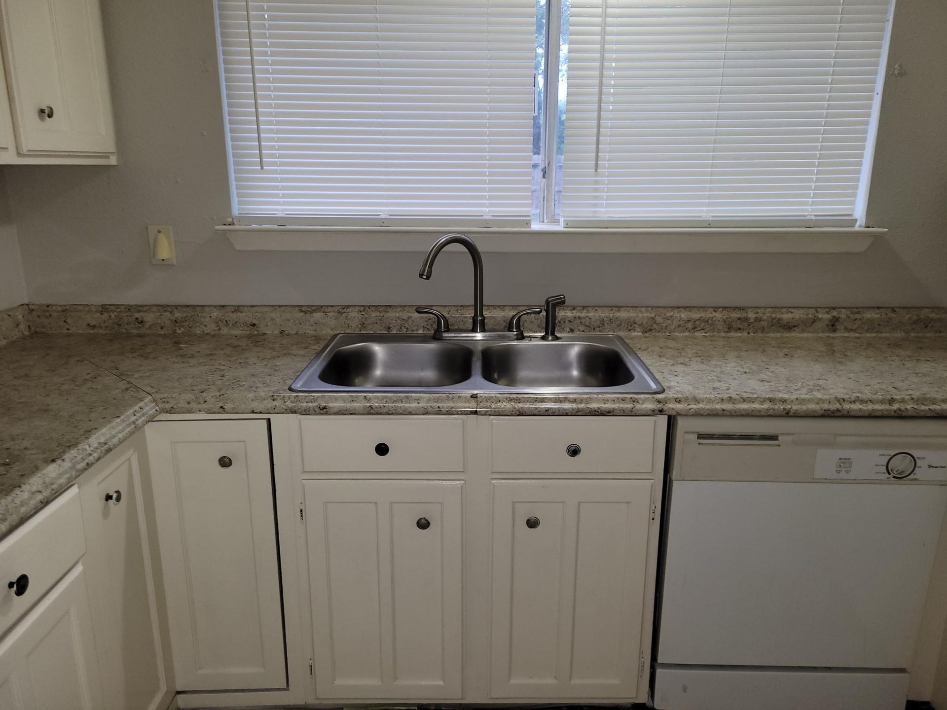 Kitchen with a double sink, white cabinets, countertop, and a window with blinds.