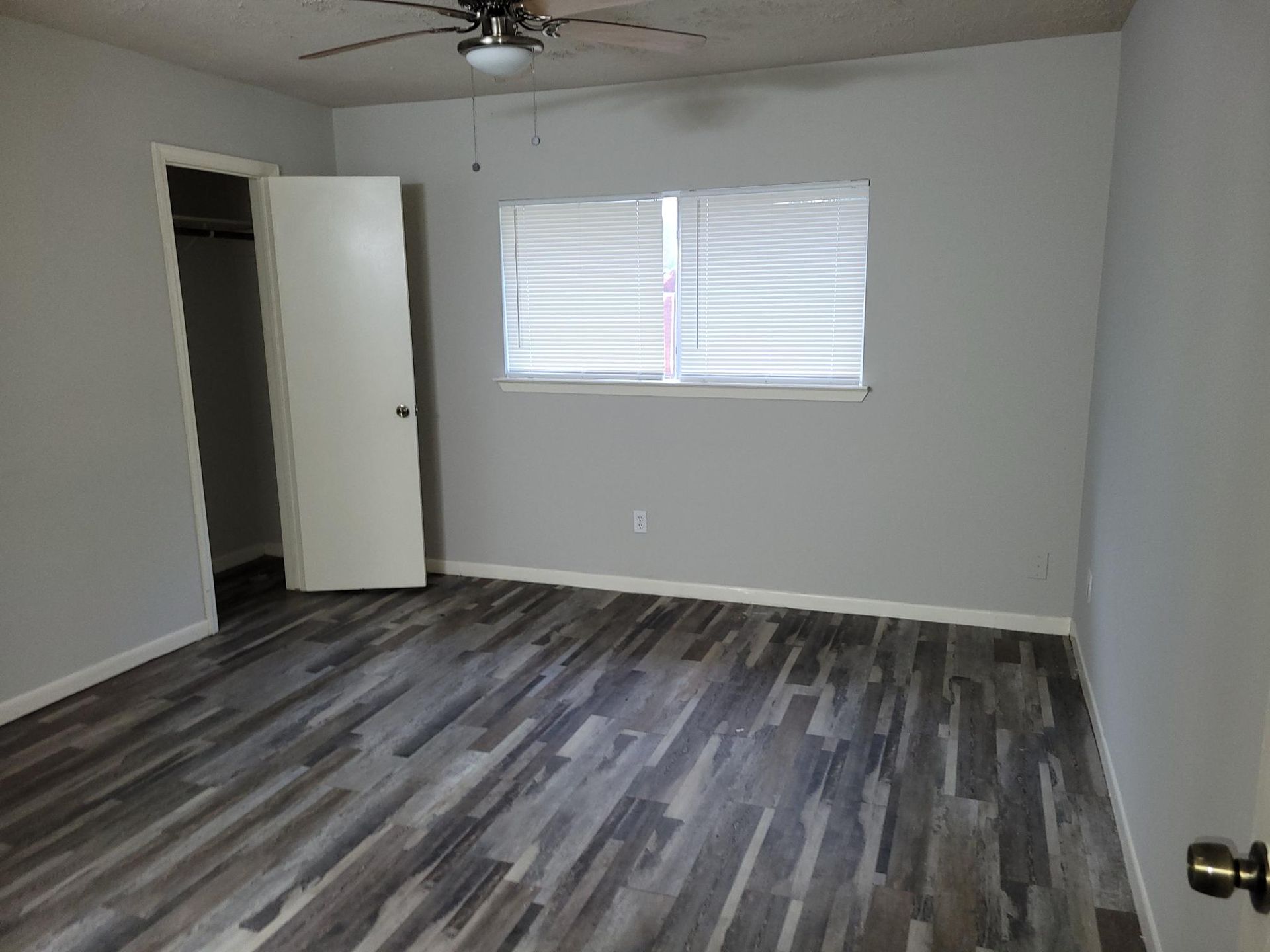 Empty bedroom with gray walls, wood-look flooring, closet, and window with blinds.