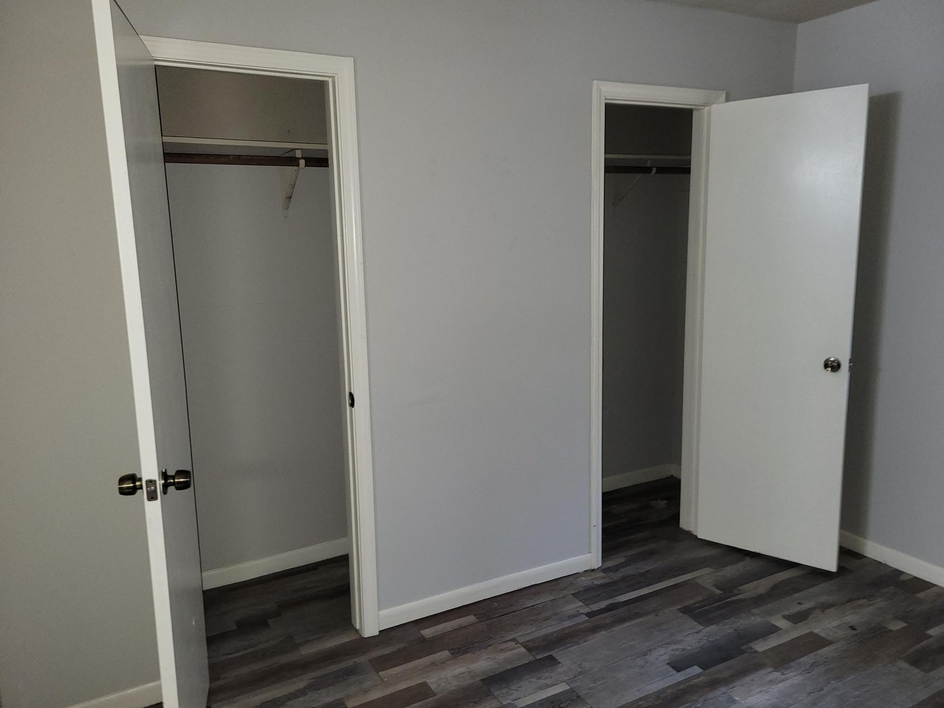 Two open white doors in a room with gray walls and wood-look flooring, showing empty closets.