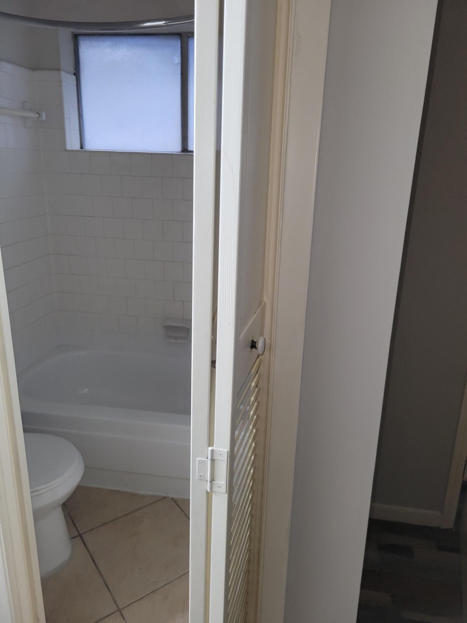 Bathroom interior with an open white door, toilet, bathtub, and window.