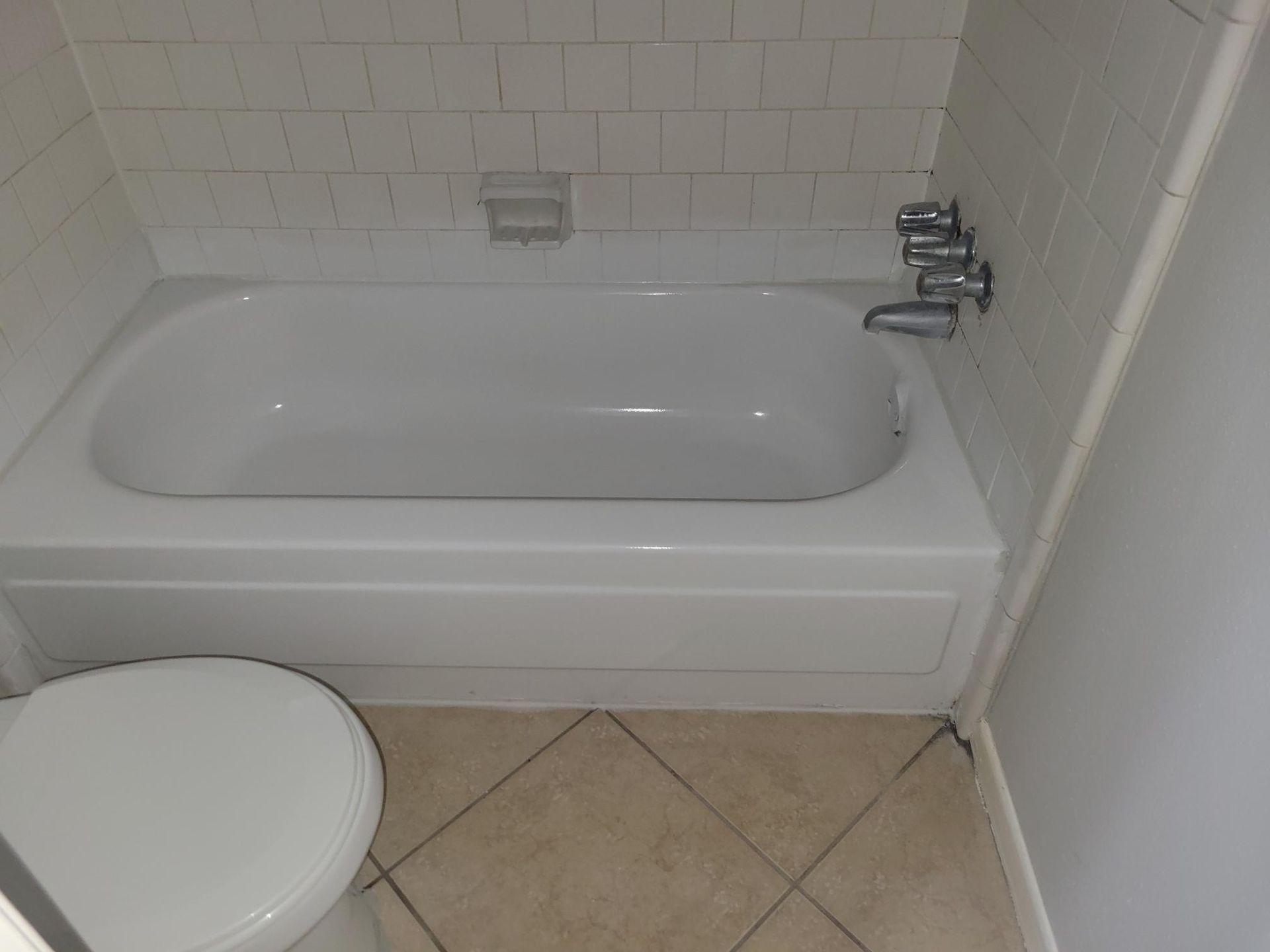 White bathtub and toilet in a tiled bathroom.