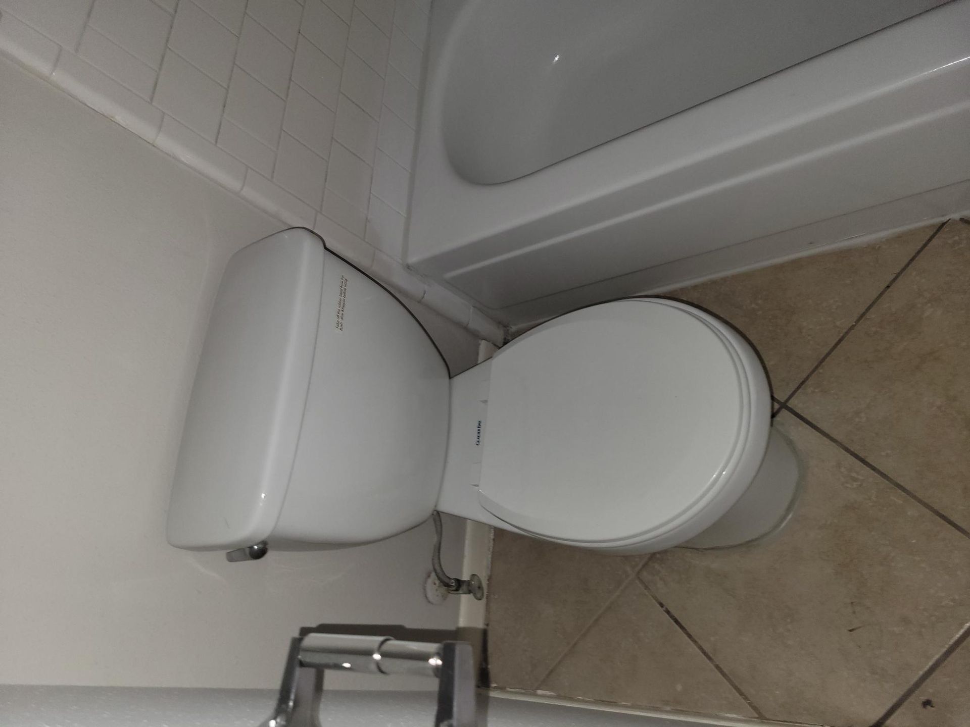White toilet in a bathroom next to a bathtub. Tan tile floor.