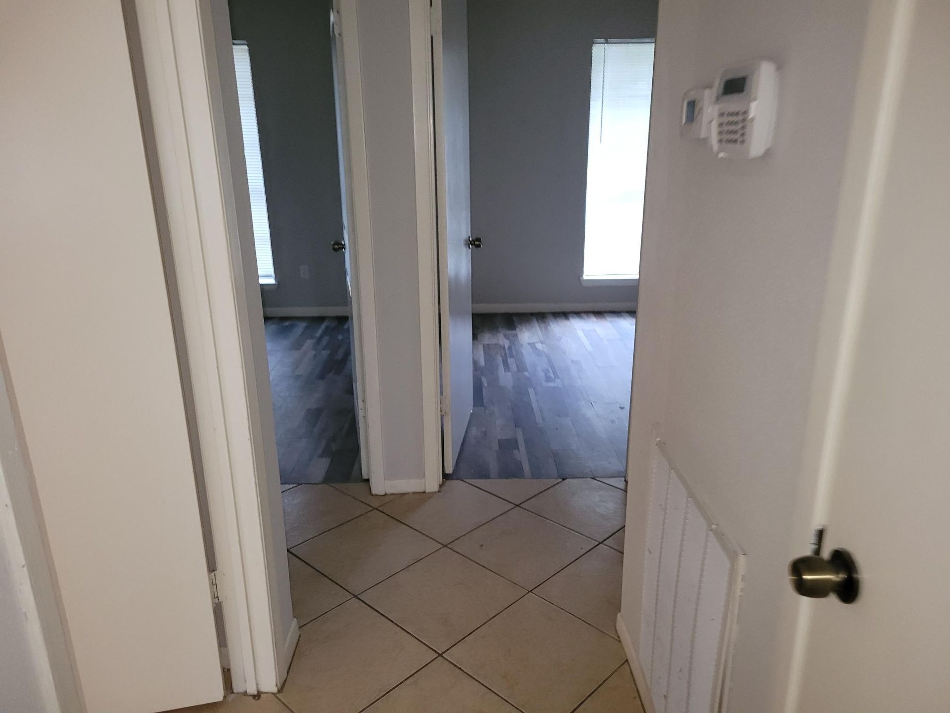 Hallway with tile floor, doorways leading to rooms with dark wood floors and windows.