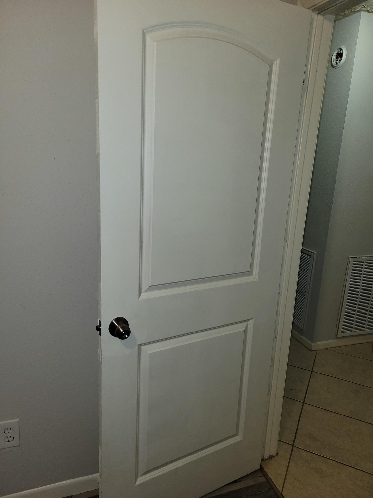 White interior door with arched panel, black doorknob, beside gray wall and open doorway.
