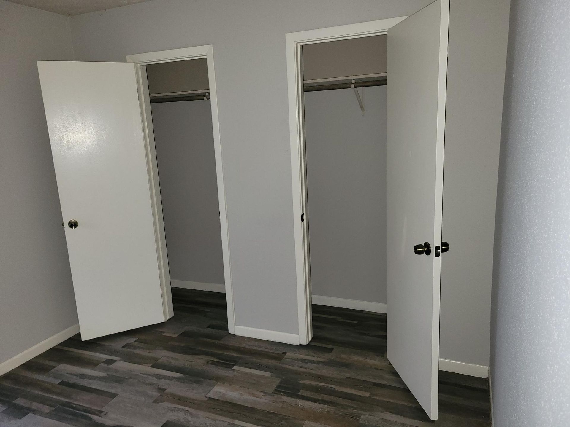 Two white closet doors open in a room with gray walls and wood-look flooring.