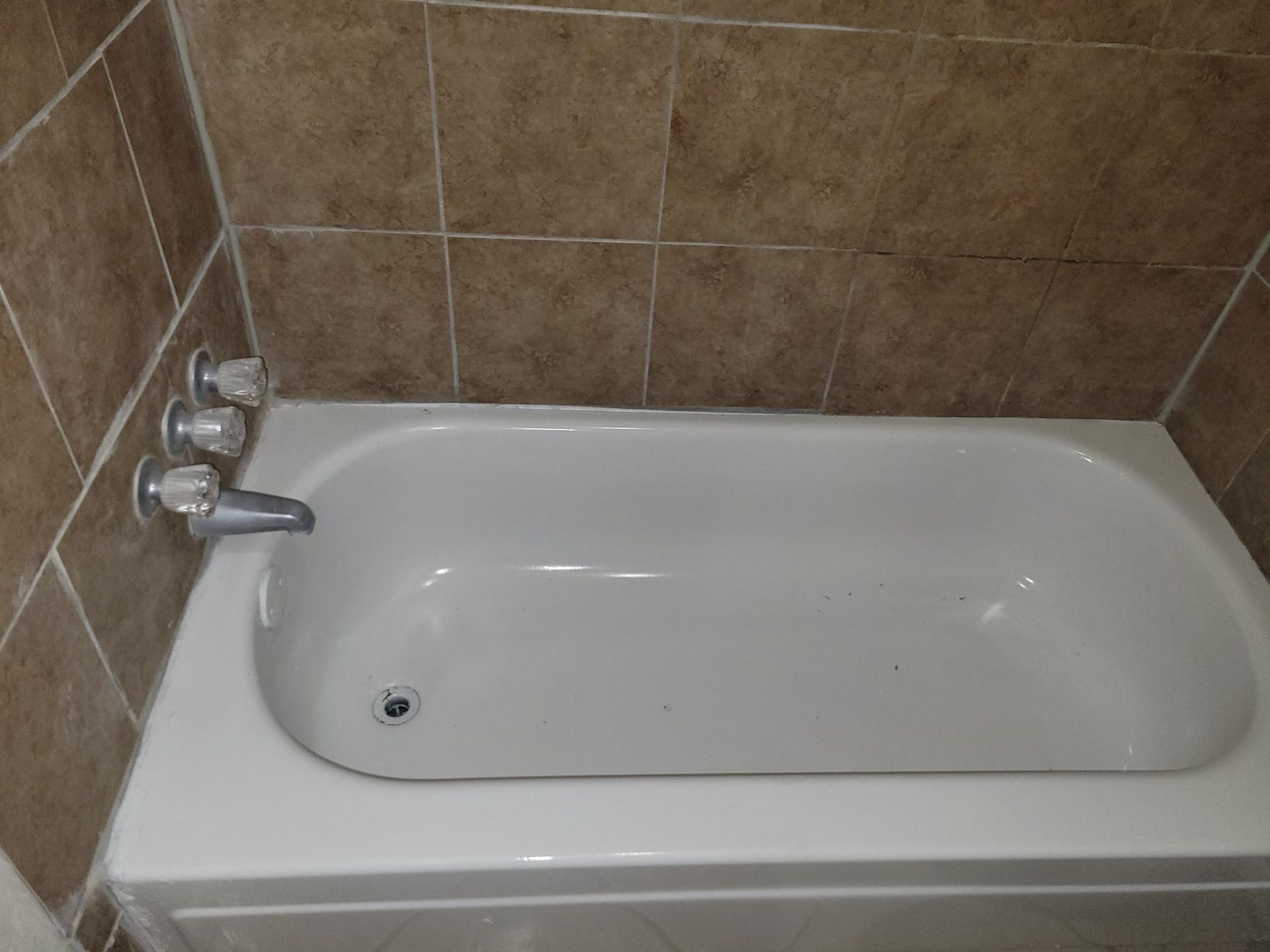 White bathtub with chrome fixtures, tan tile surround.