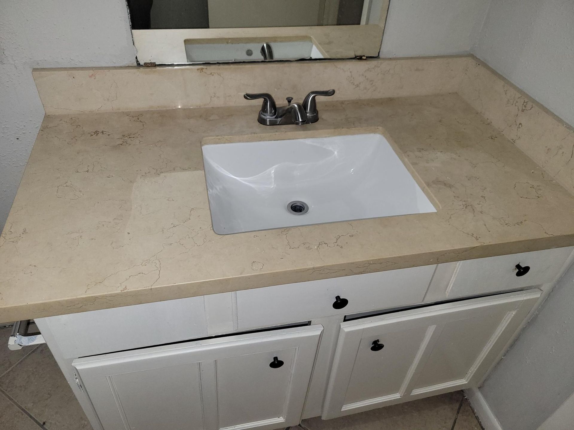 Bathroom vanity with a white sink, beige countertop, and white cabinets.