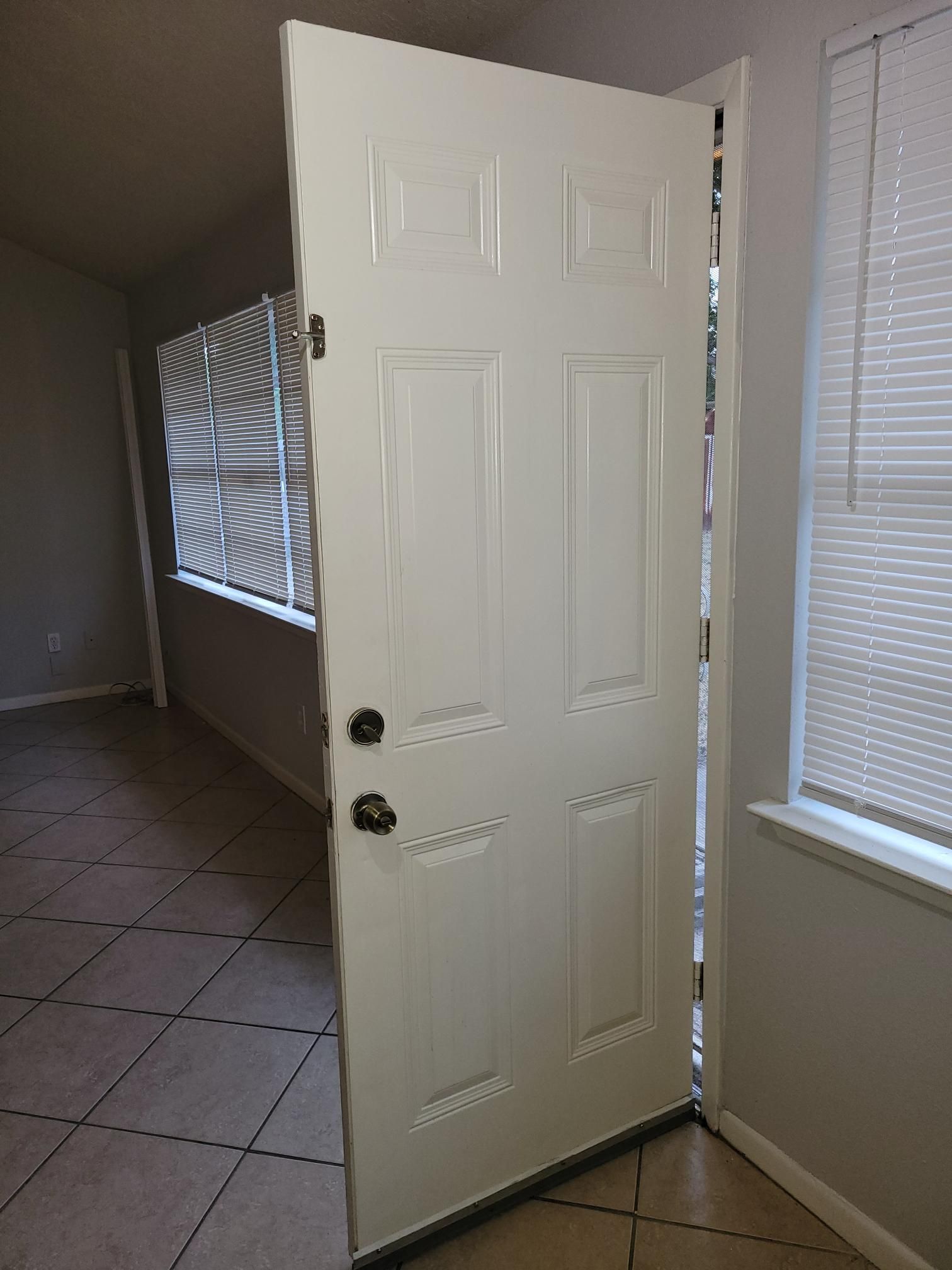 White door ajar, revealing a hallway with a window, tile floor, and a second window to the right.