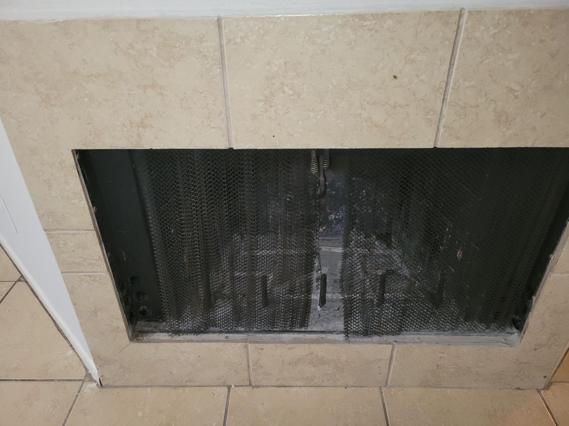 Fireplace with a metal mesh screen, surrounded by beige tile.