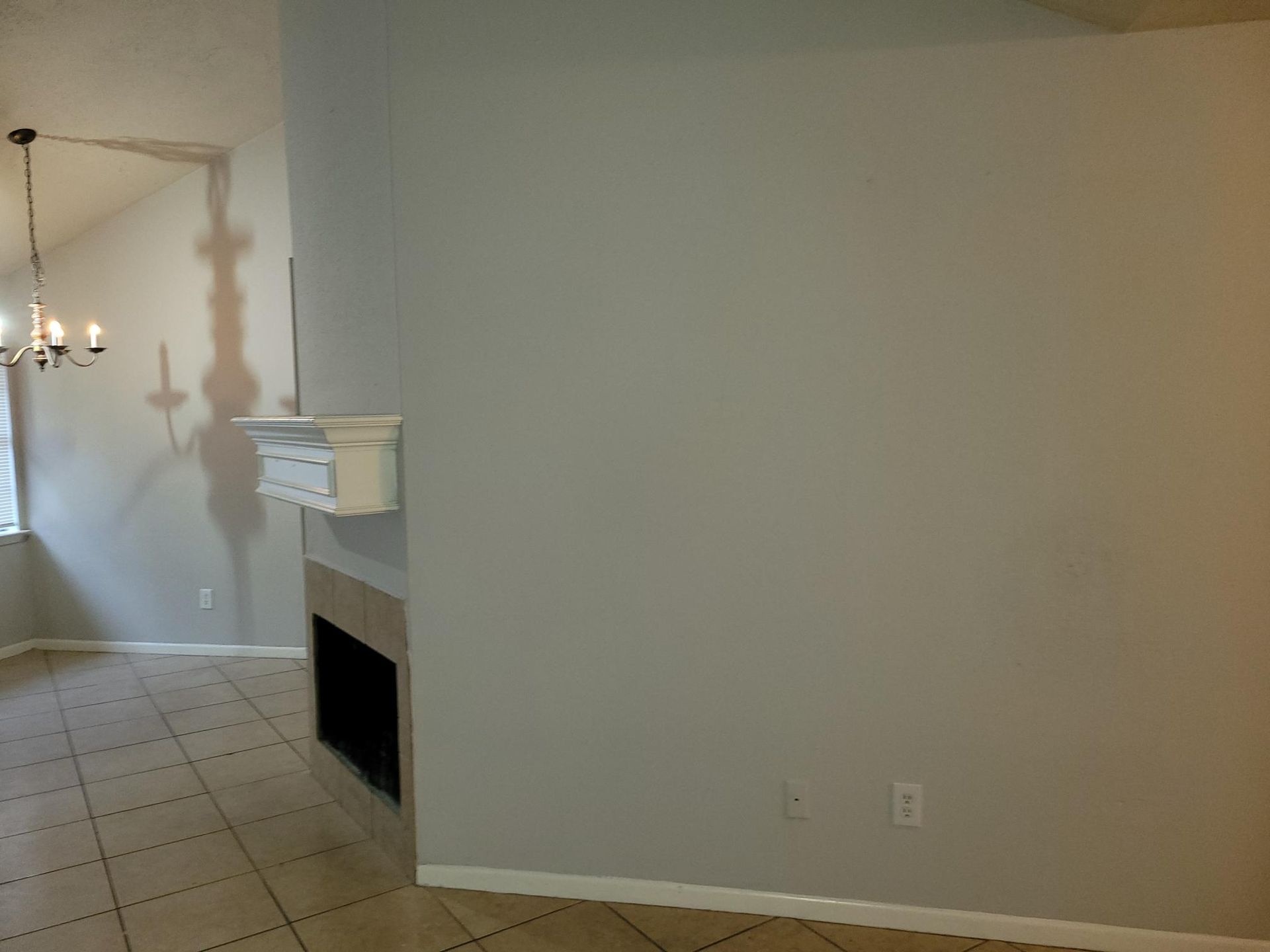 Living room with fireplace, gray walls, chandelier, and tile floor.