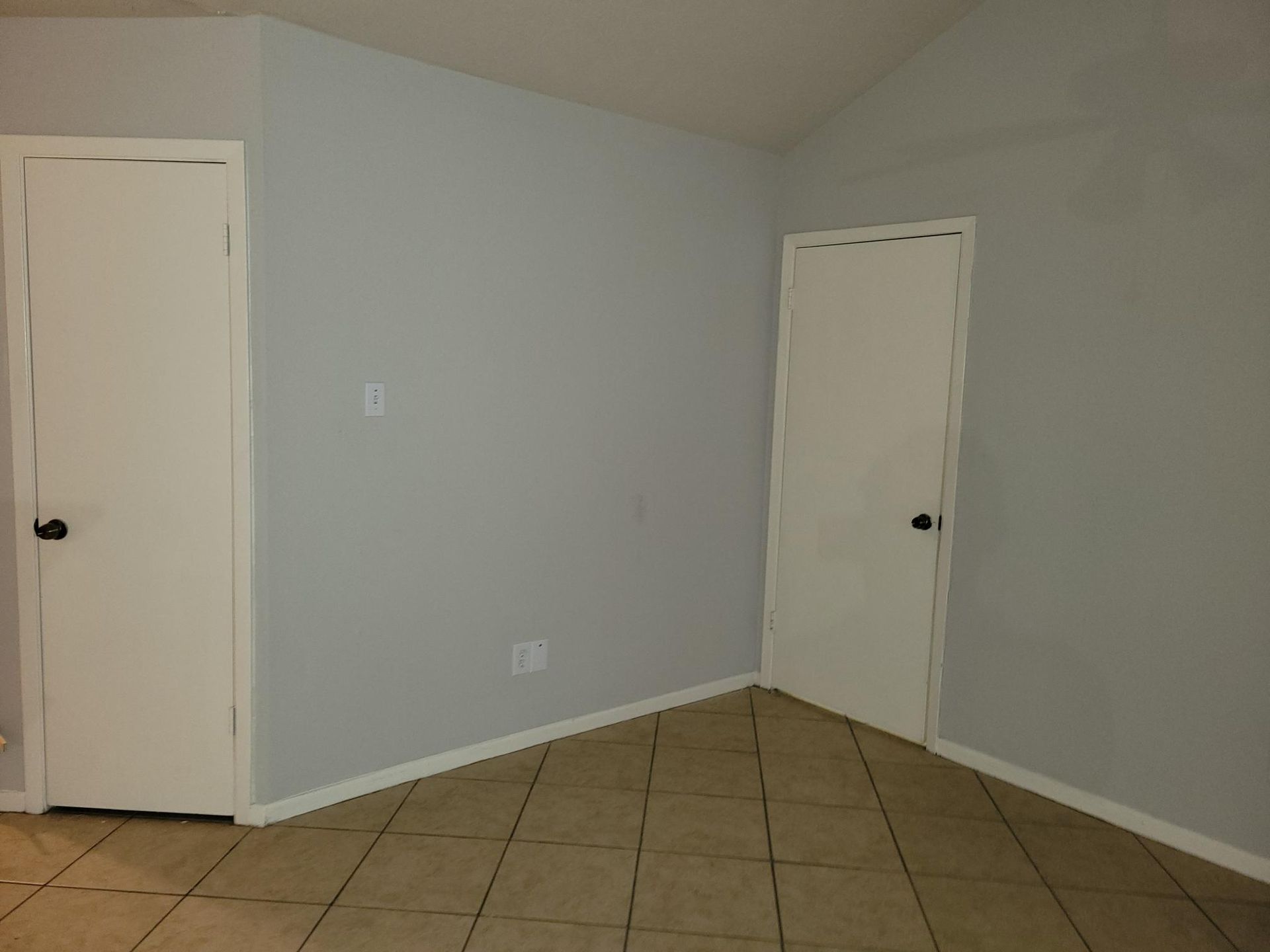 Empty room with two white doors, gray walls, and tiled floor.