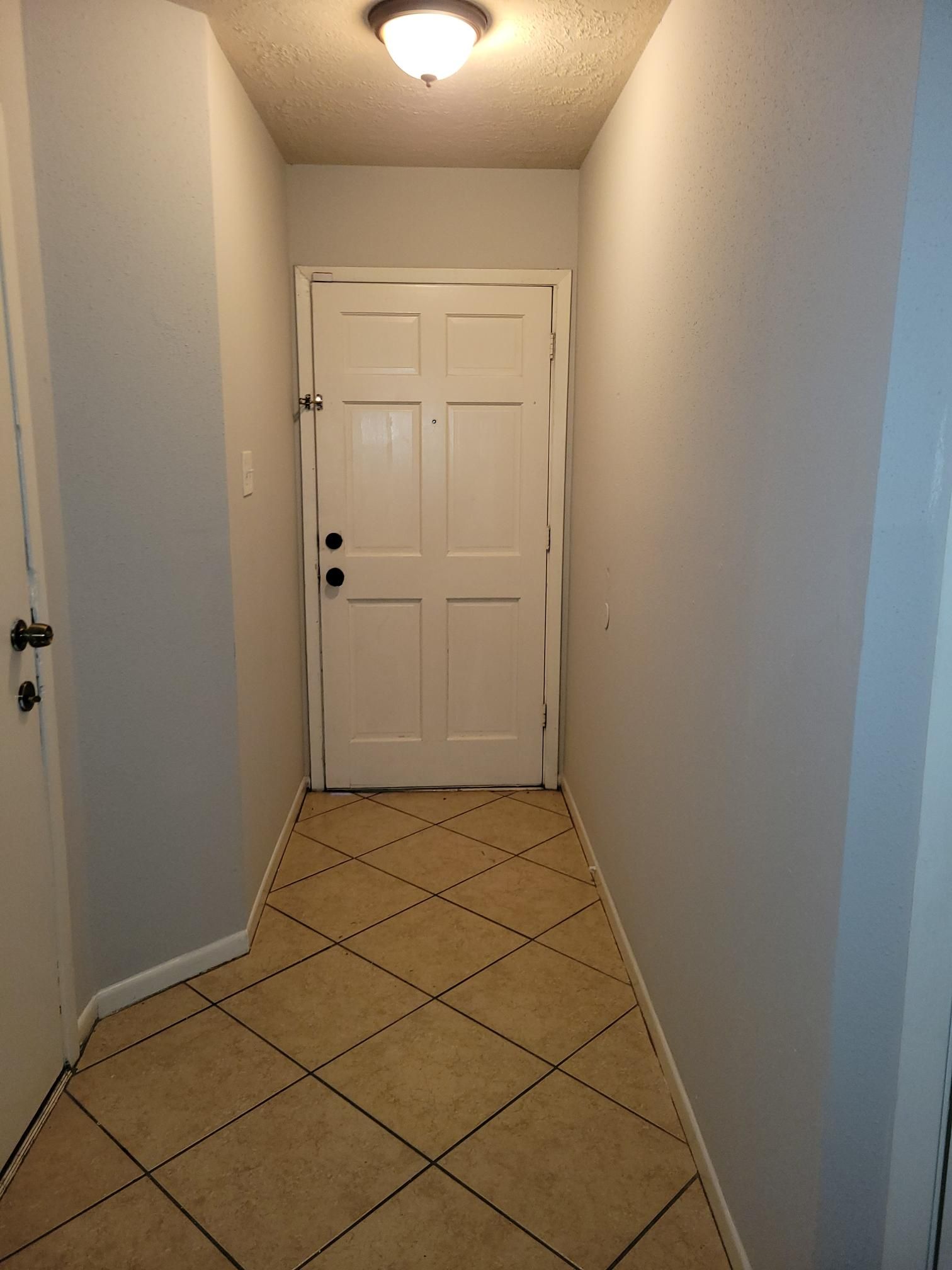 Narrow hallway with light gray walls, white door, and tiled floor.