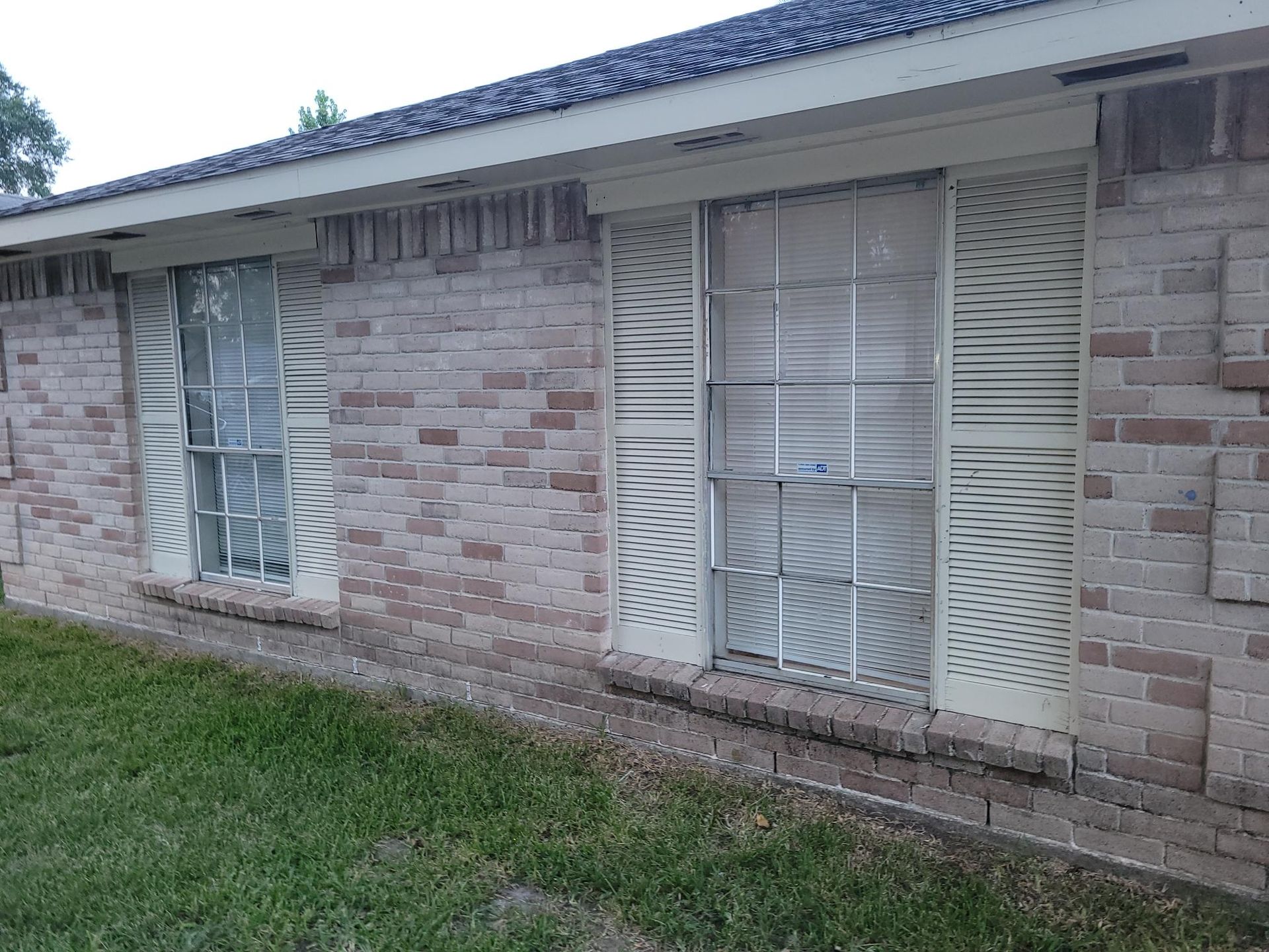 Exterior of a brick building with two windows featuring security bars and cream-colored shutters.