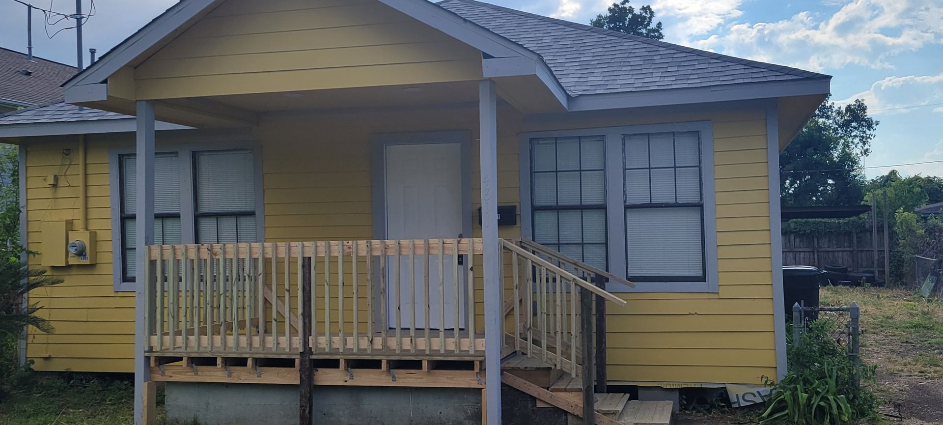 Yellow house with porch and wooden railing. Gray roof, gray trim, and white door.