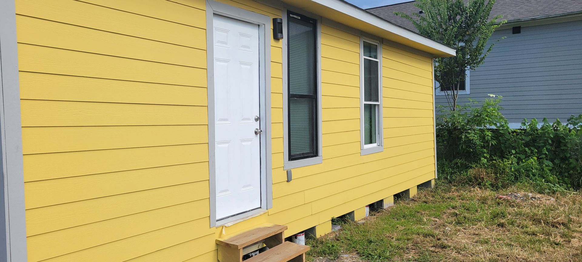 Yellow building with a white door and windows; green grass in front.