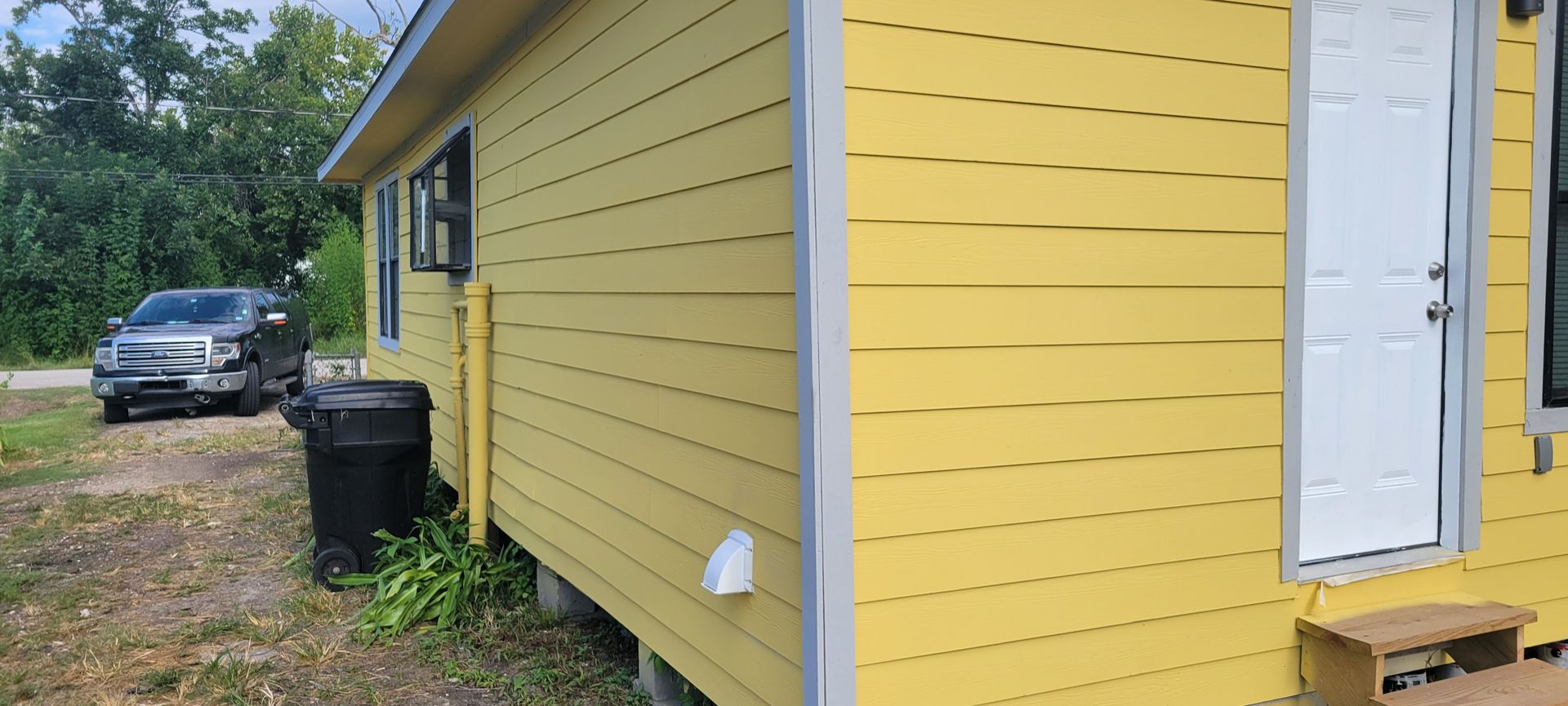 Yellow house with white door and silver car parked in front.