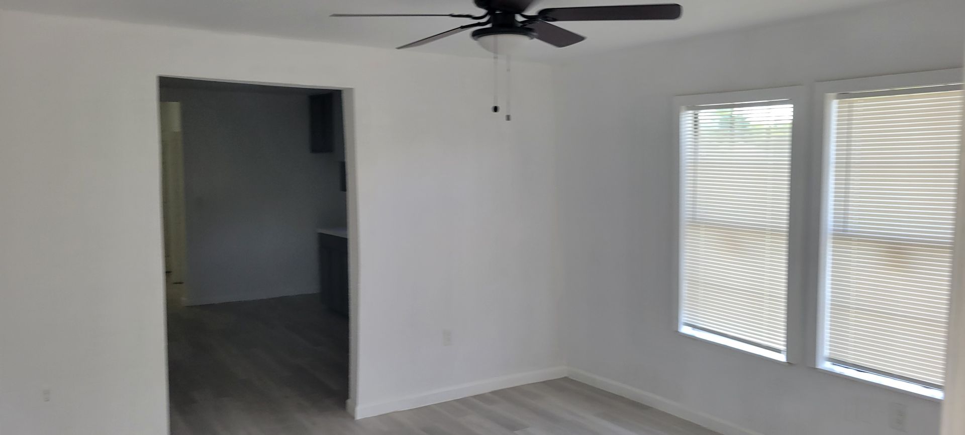 Empty room with white walls, a doorway, window, ceiling fan, and light-colored flooring.