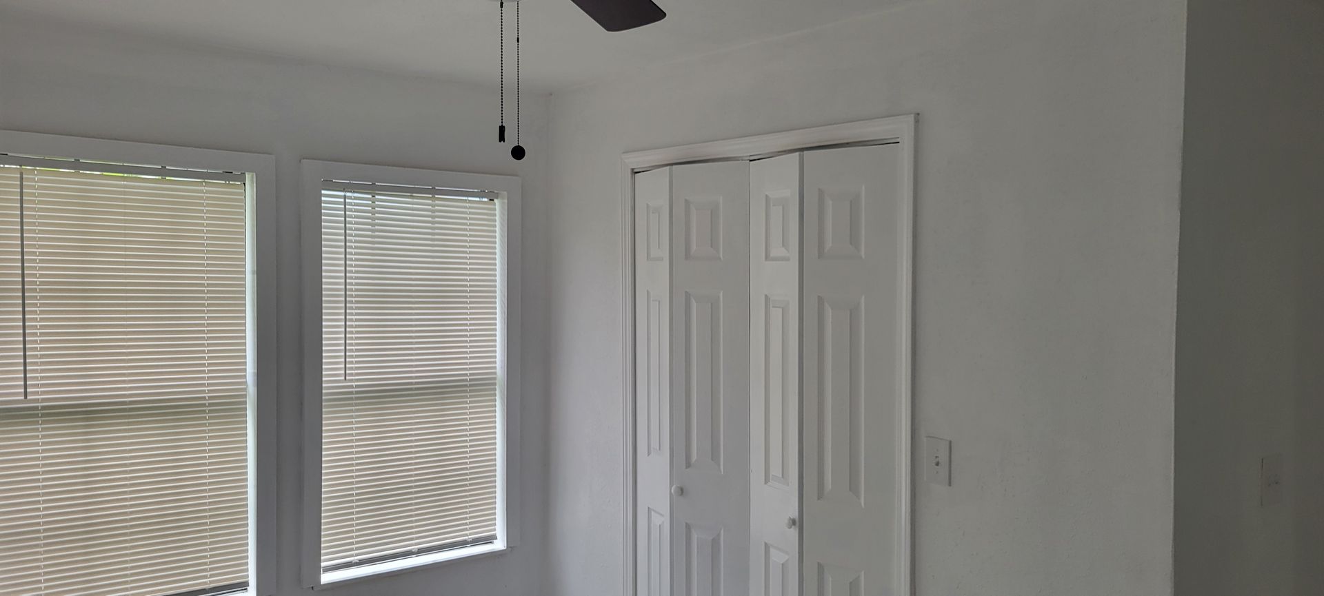 A room with a white ceiling, walls, closet doors, and blinds over a window.