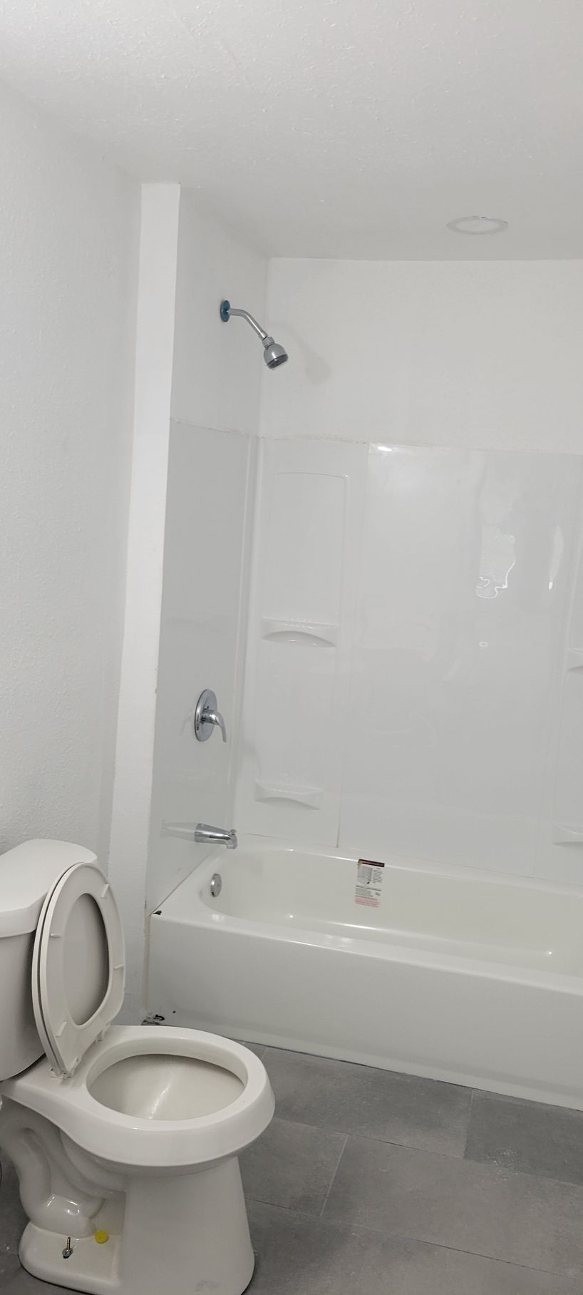 Bathroom with white walls and fixtures, toilet in the foreground, shower/tub combo.