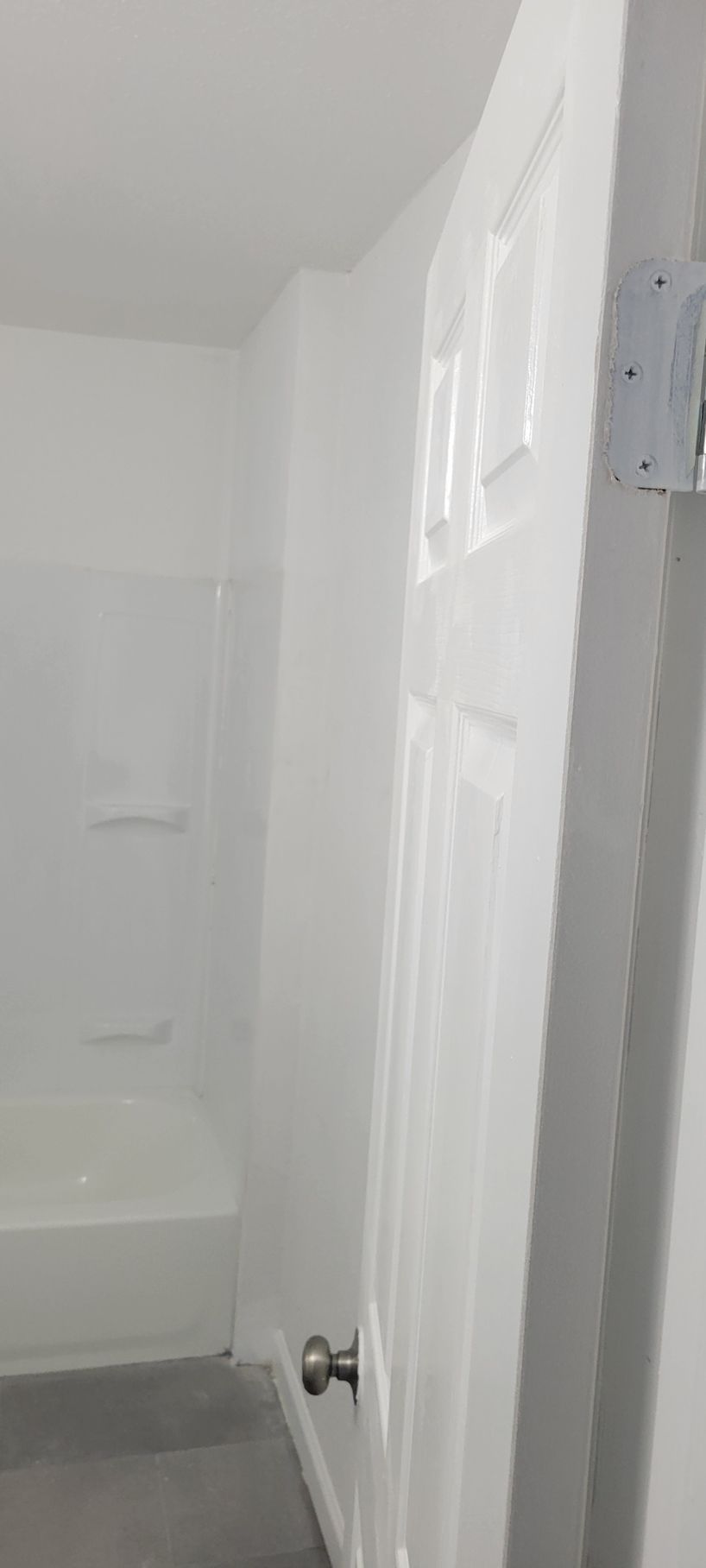 White bathroom interior with a shower, door, and grey floor.