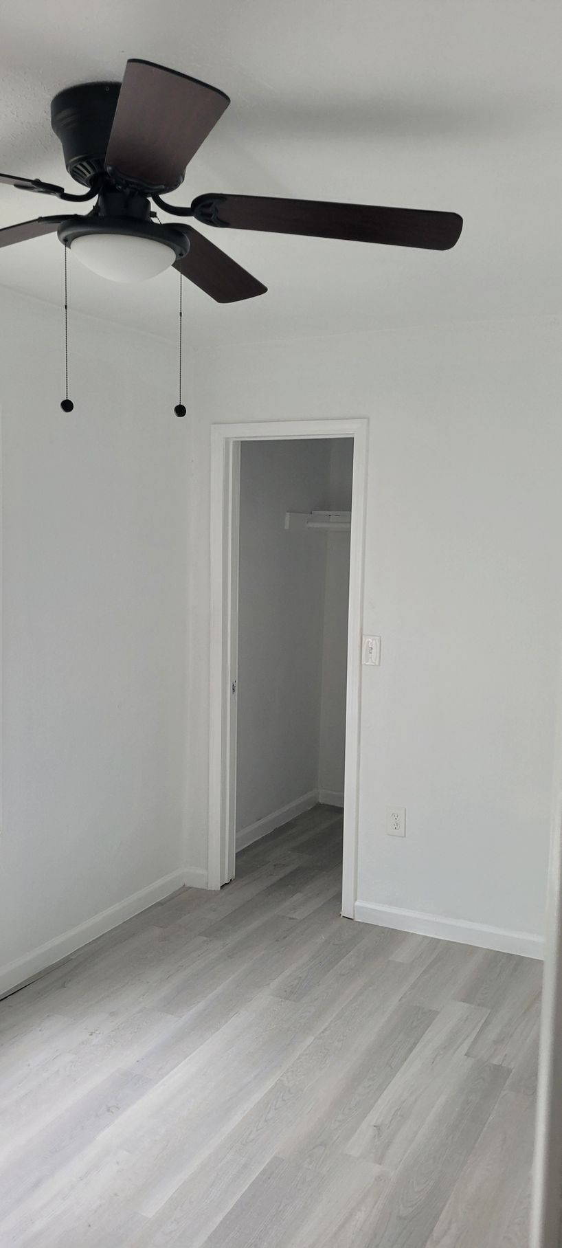 A room with light gray flooring and white walls, a doorway leads to a closet, and a ceiling fan is mounted.