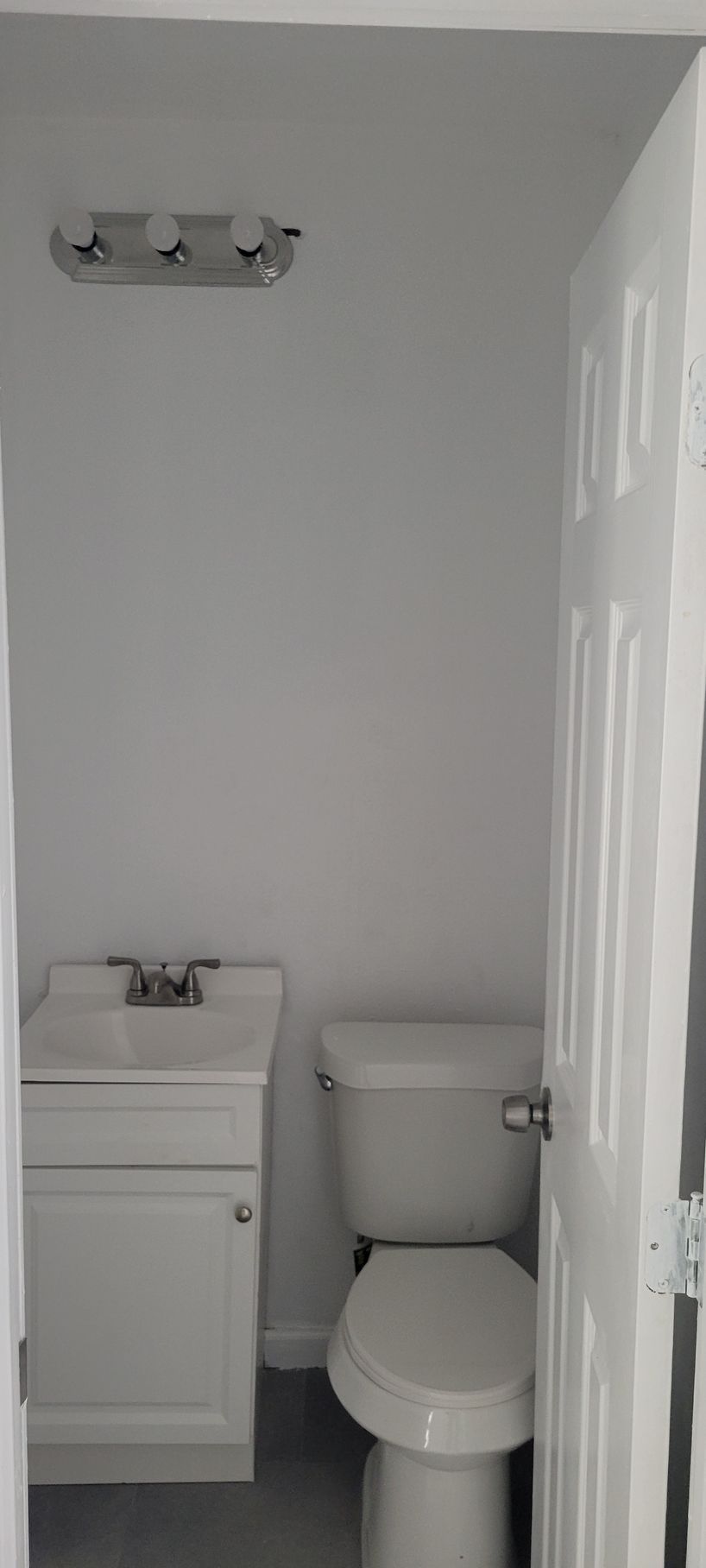 Small bathroom with a toilet, sink, and overhead light fixture. White door slightly ajar.