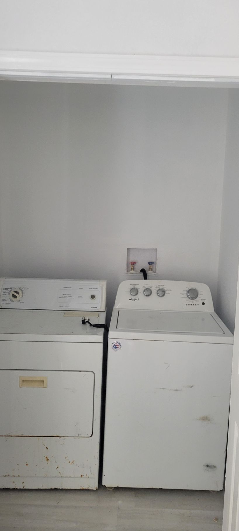 A white dryer and washing machine sit in a small laundry area with neutral walls.