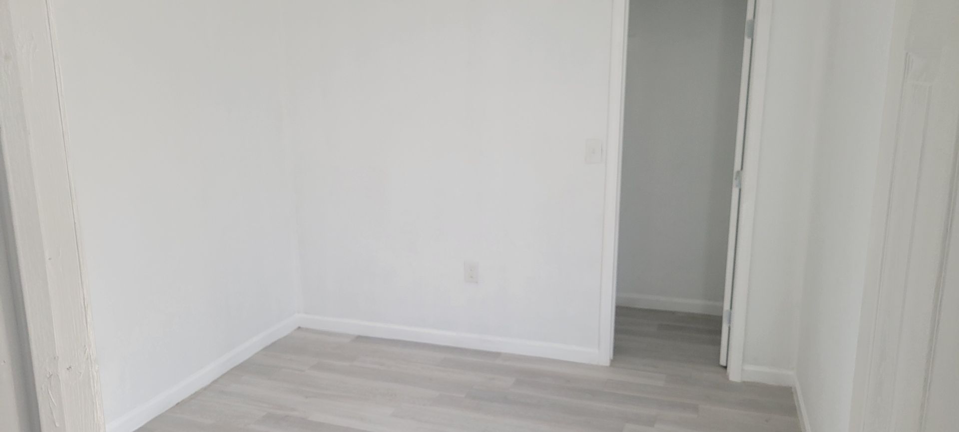 Empty room with white walls, baseboards, and light gray flooring.  An open doorway is visible.