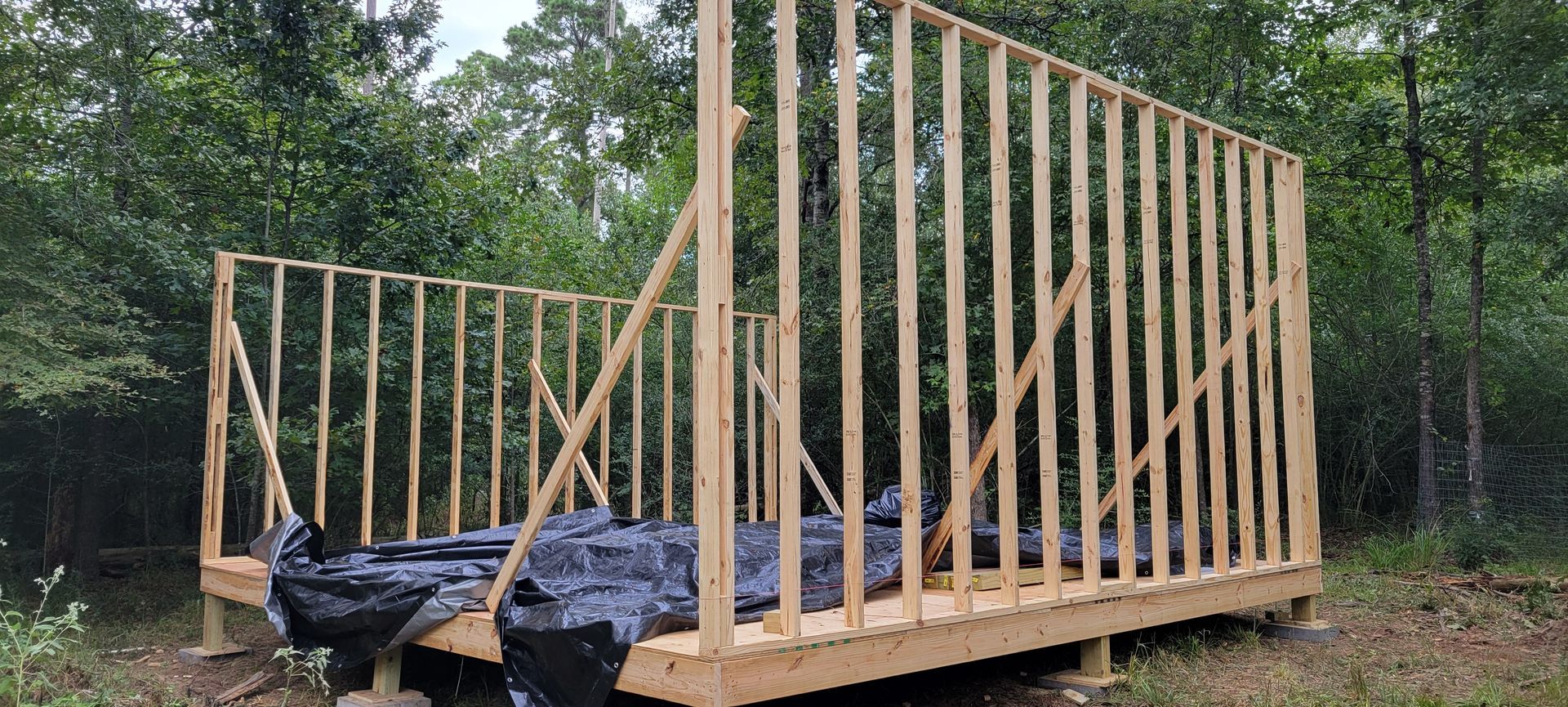 Wooden structure of a small building under construction, surrounded by trees.