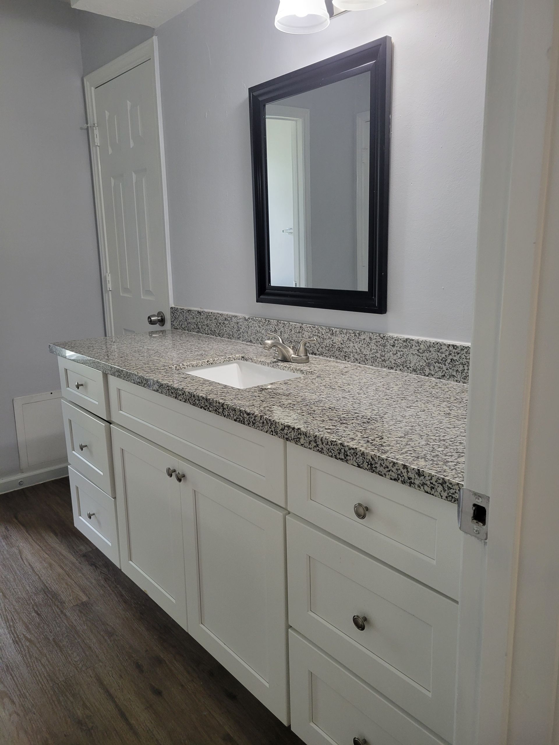 Bathroom with white cabinets, granite countertop, and framed mirror.