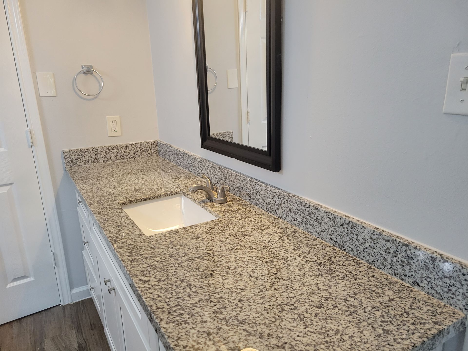 Bathroom with gray countertop, white cabinets, and a black-framed mirror.
