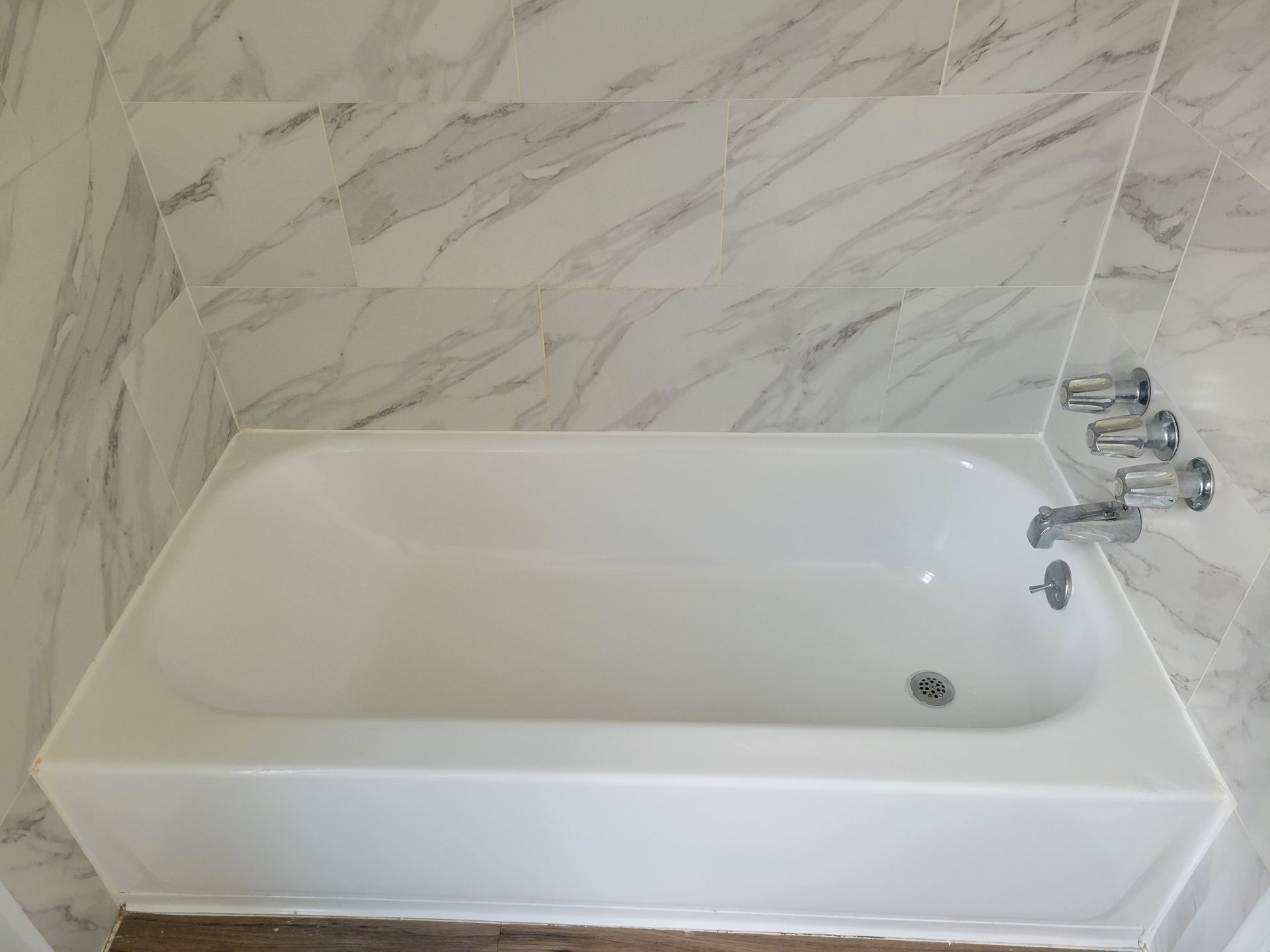 White bathtub with chrome fixtures and marble tile wall.