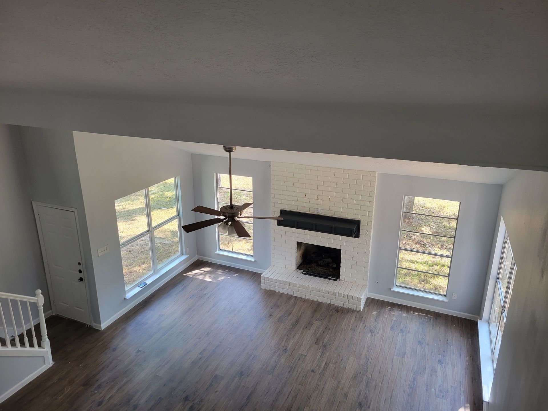 Overhead view of a living room with windows, a fireplace, and a ceiling fan, painted white and grey.