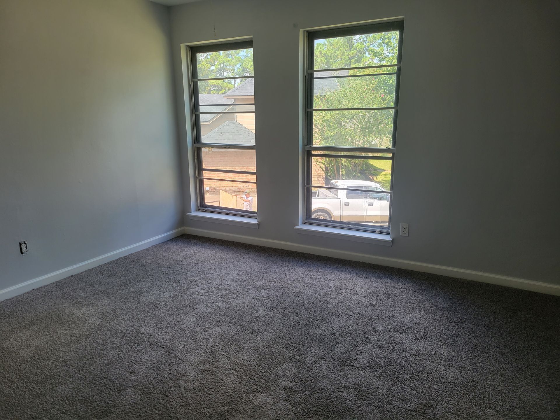 Empty bedroom with gray walls, two windows, and gray carpet.