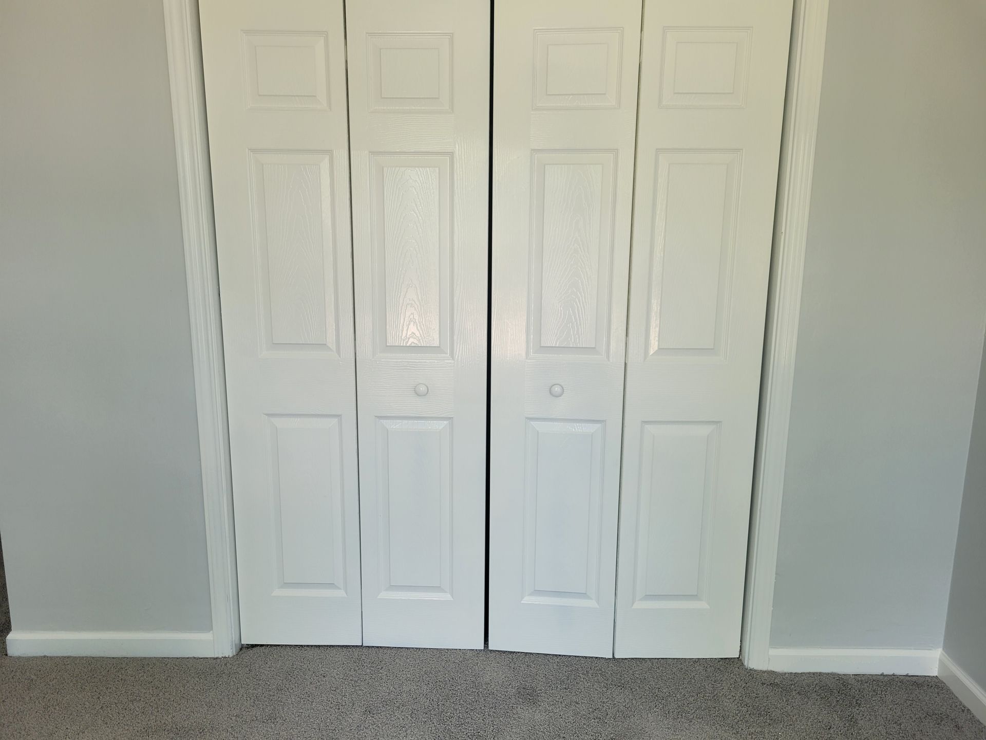 White bi-fold closet doors set in a gray wall and above a gray carpet.