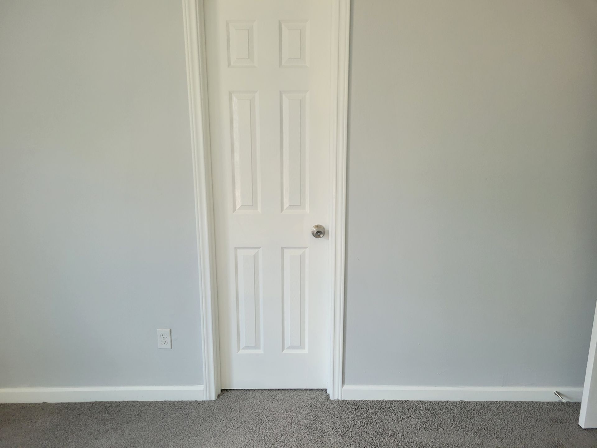 White door in a gray-walled room with a gray carpet and white baseboards.