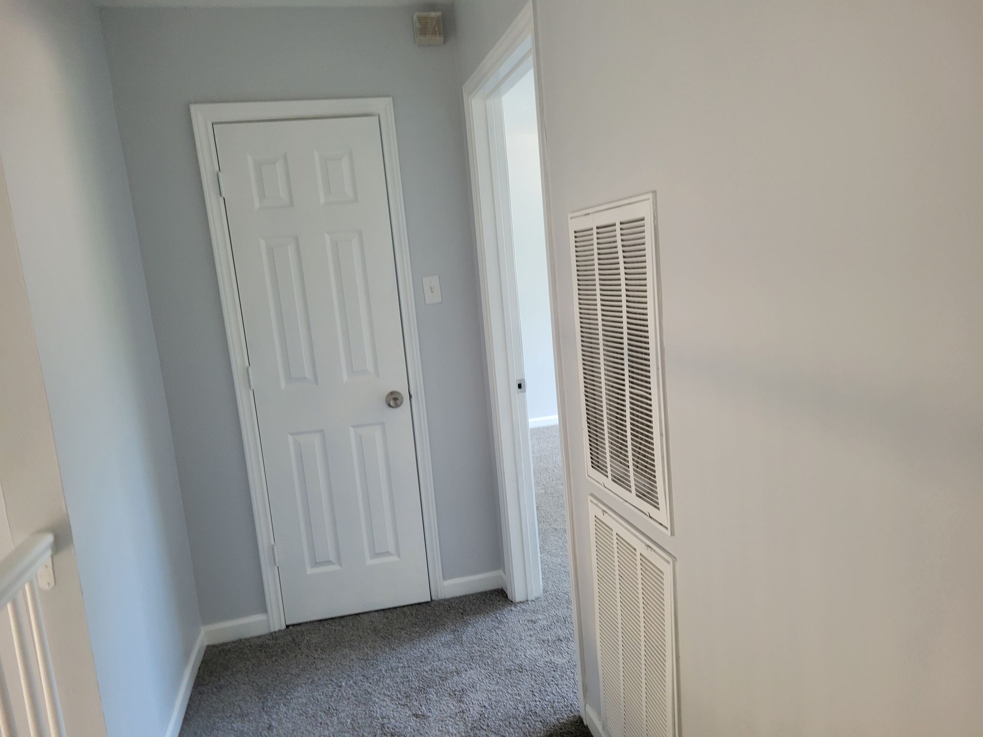 Hallway with white door, gray carpet, and air vent.