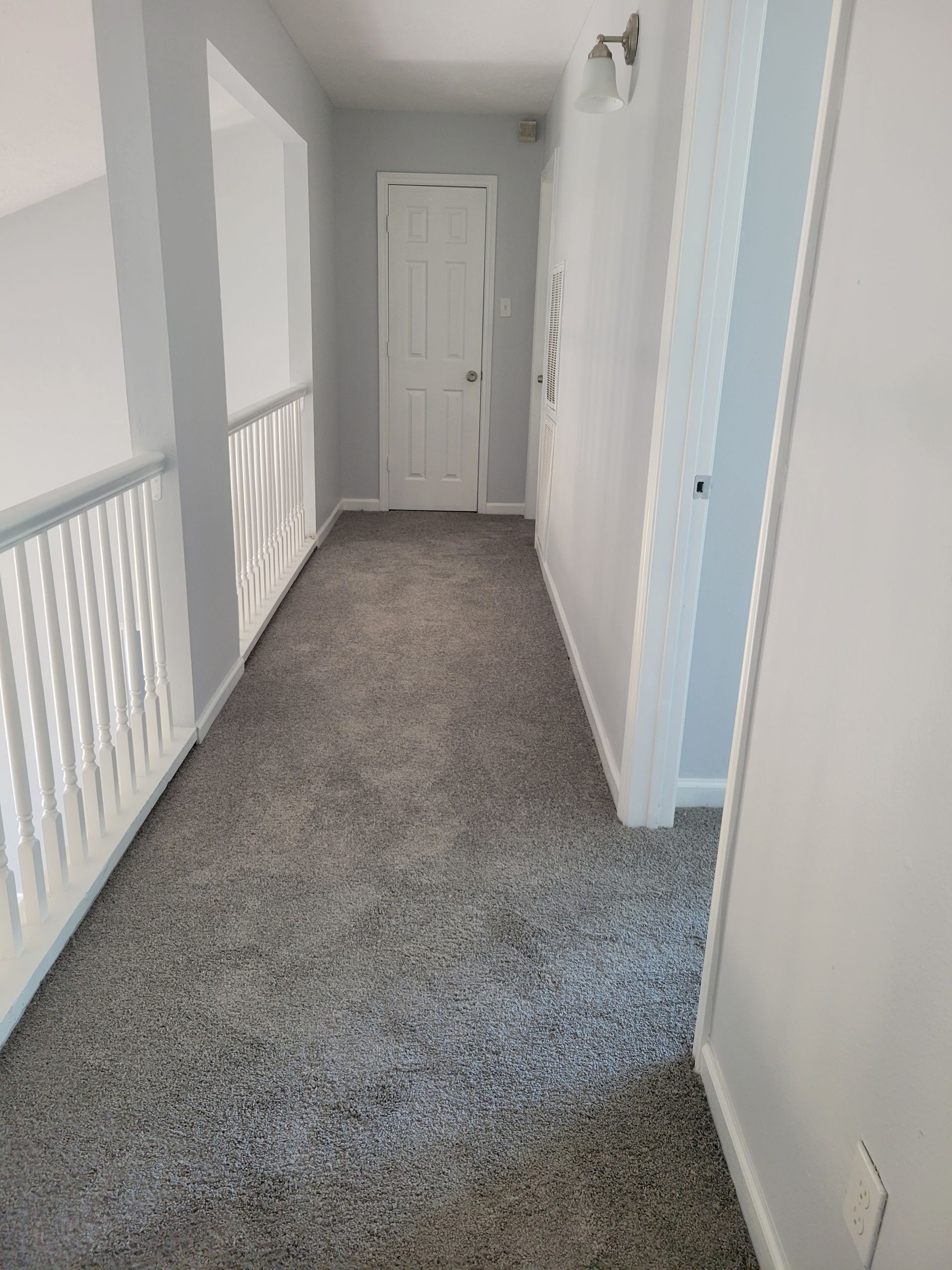 Hallway with gray carpet, white walls, and a closed door.