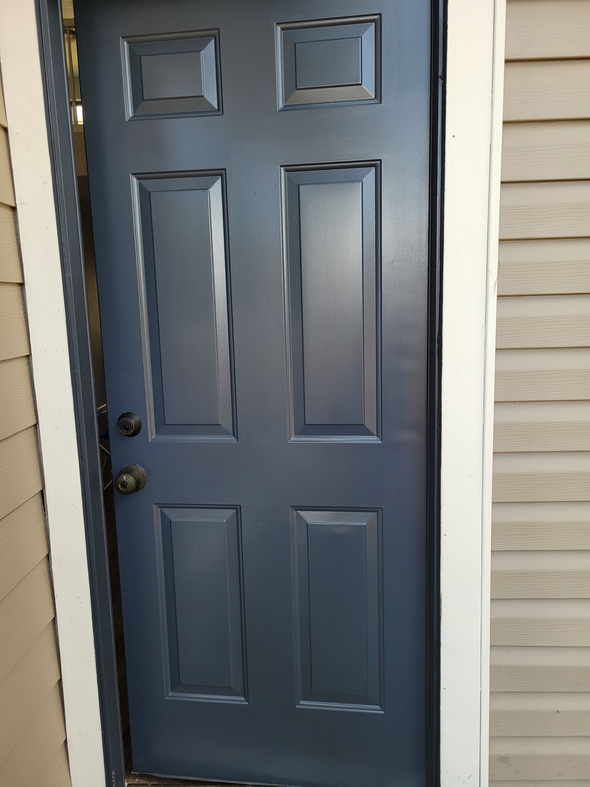 Blue six-panel door with black hardware, set in a white-trimmed doorway between beige siding.
