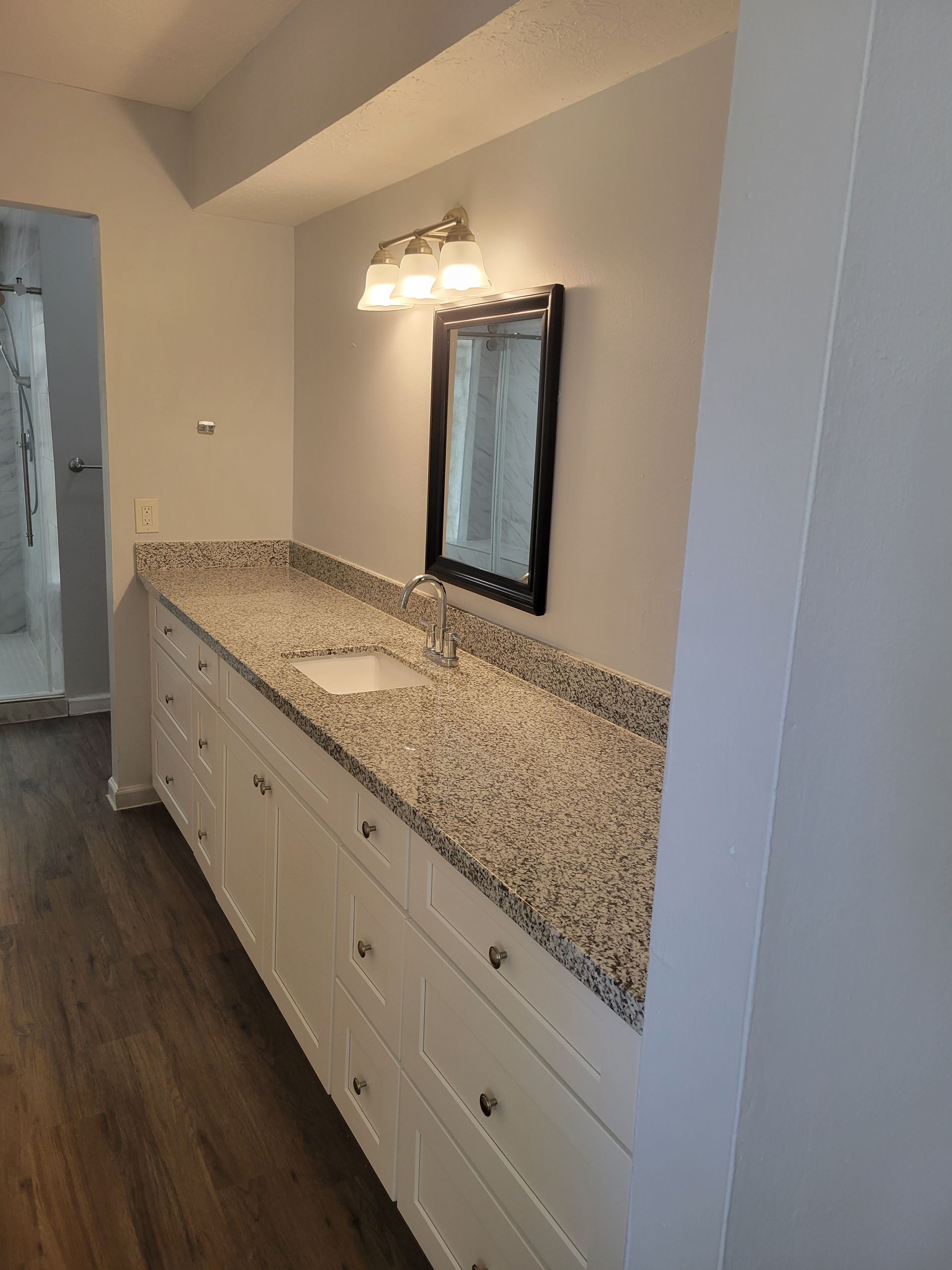 Bathroom with white cabinets, speckled countertop, rectangular mirror, and light fixture.