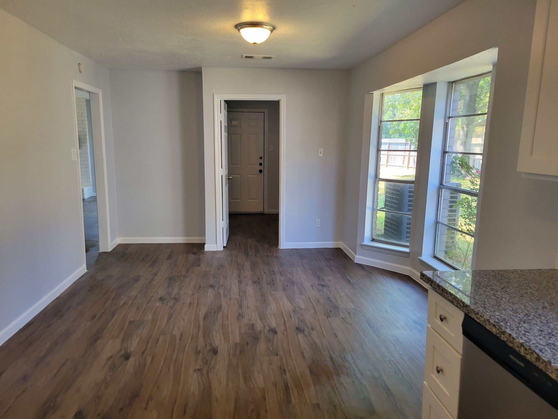 Empty dining area with wood-look flooring, neutral walls, and a window overlooking a tree.