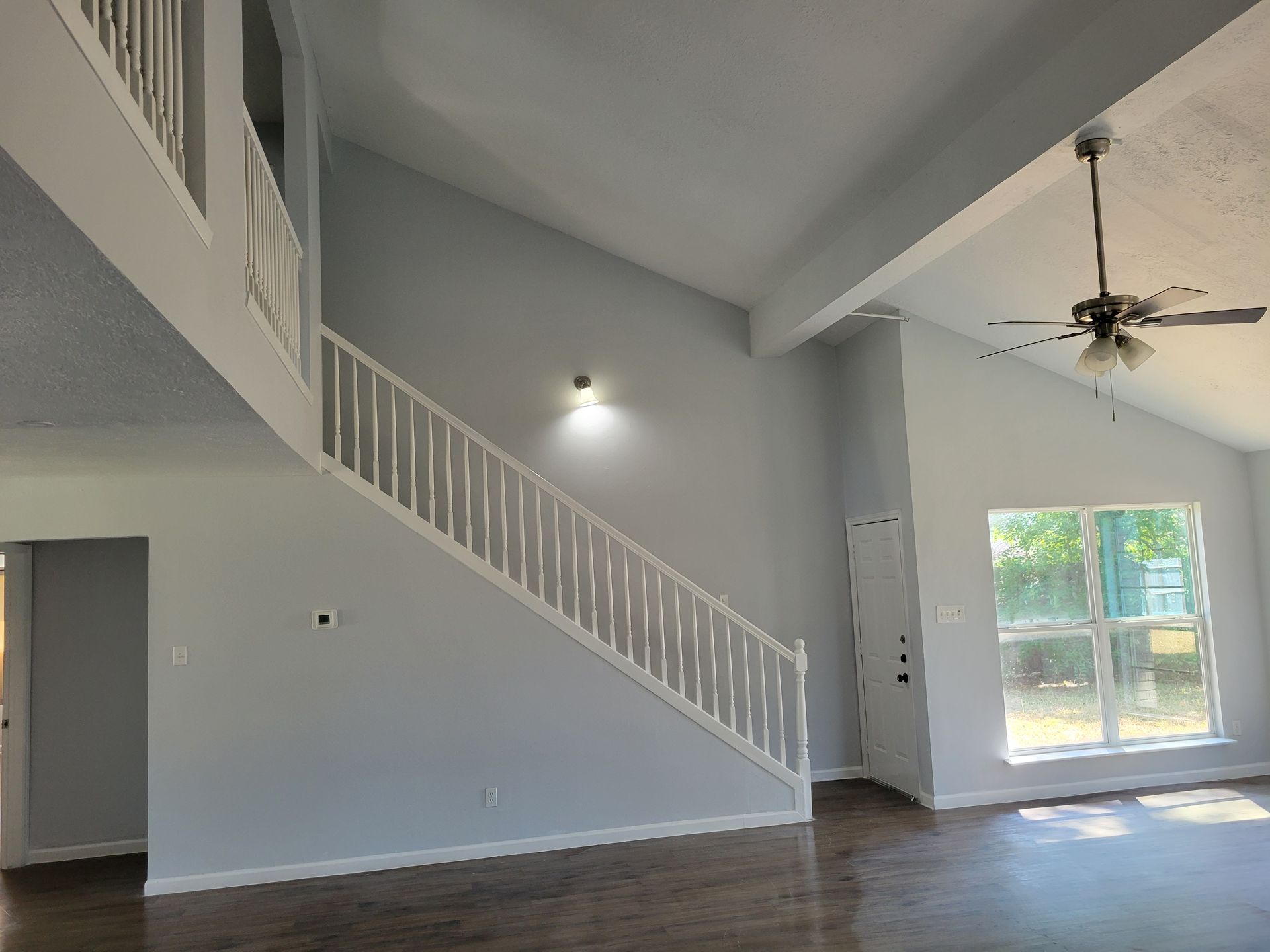 Interior view of a two-story home with stairs, light blue walls, and a ceiling fan.