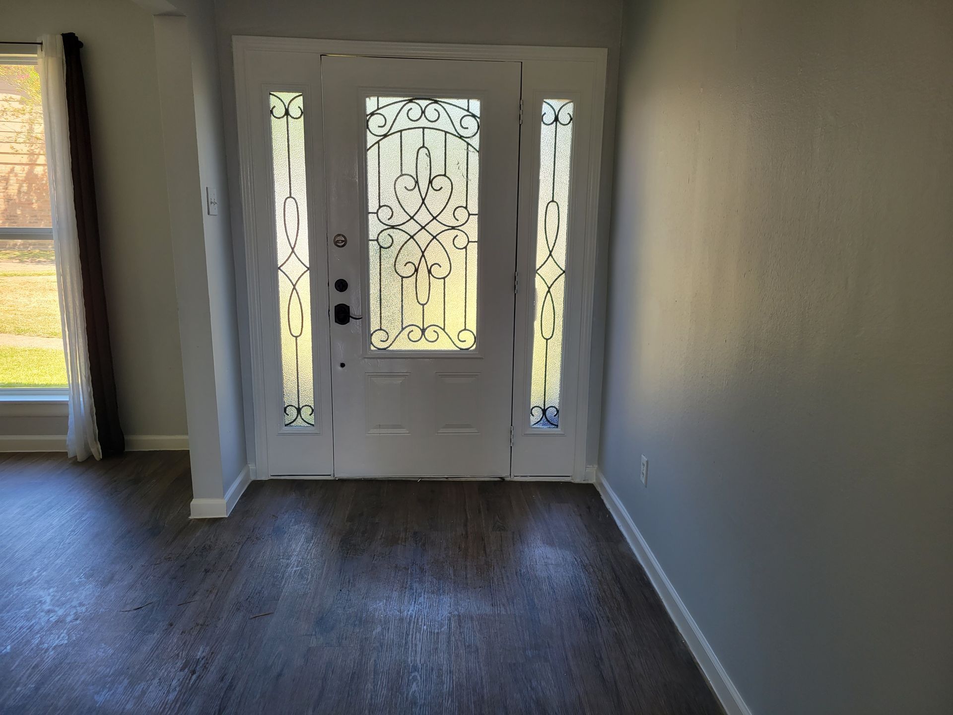 White front door with decorative glass panes. Gray walls and wood-look flooring in a home interior.