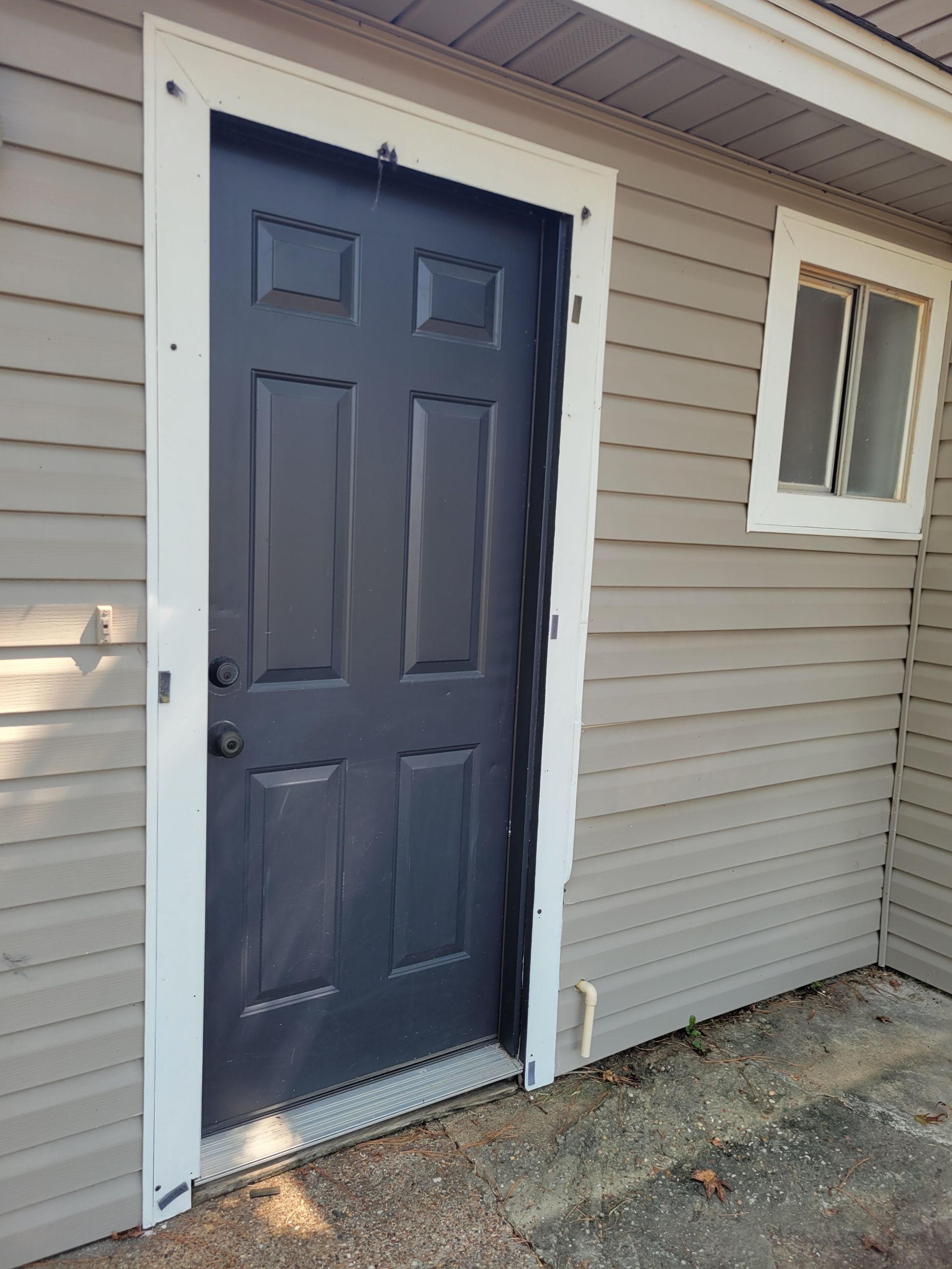 Dark gray exterior door with white trim on a light gray siding building.
