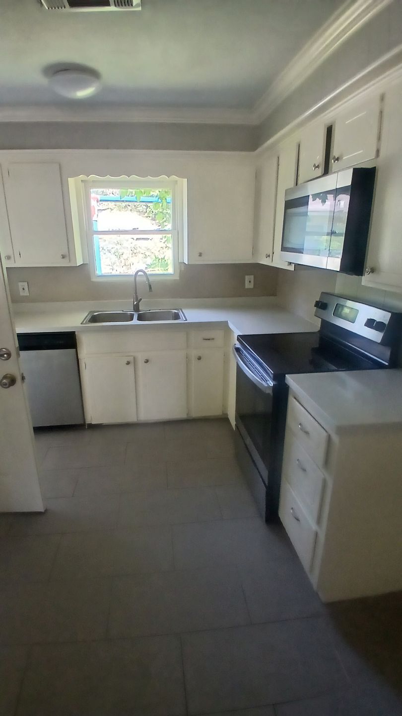 White kitchen with cabinets, sink, window, stove, microwave, and dishwasher.