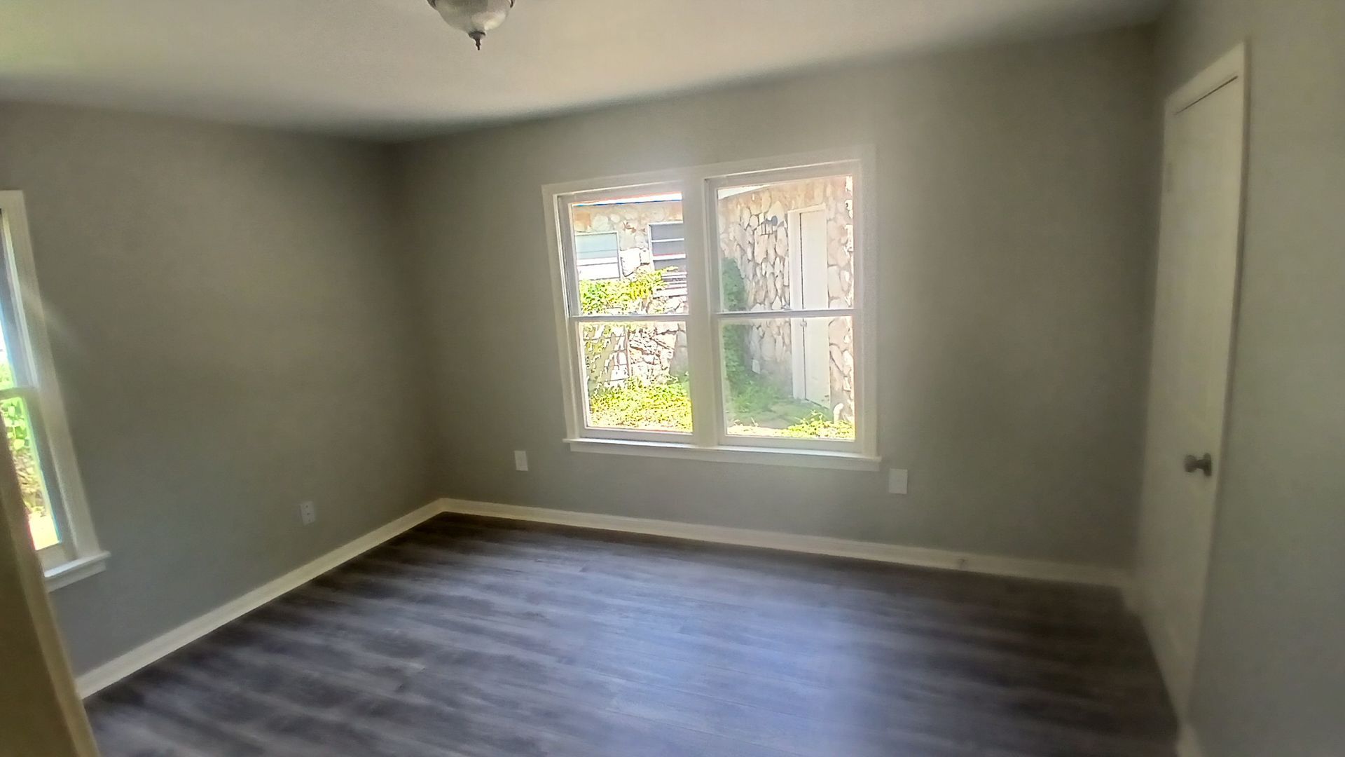 Empty bedroom with gray walls, dark wood-look floor, and two windows.