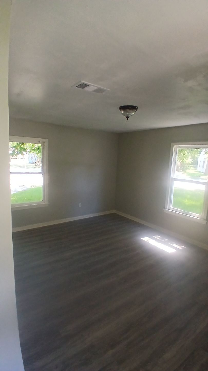 Empty room with gray walls, dark wood-look floor, two windows, and ceiling light.